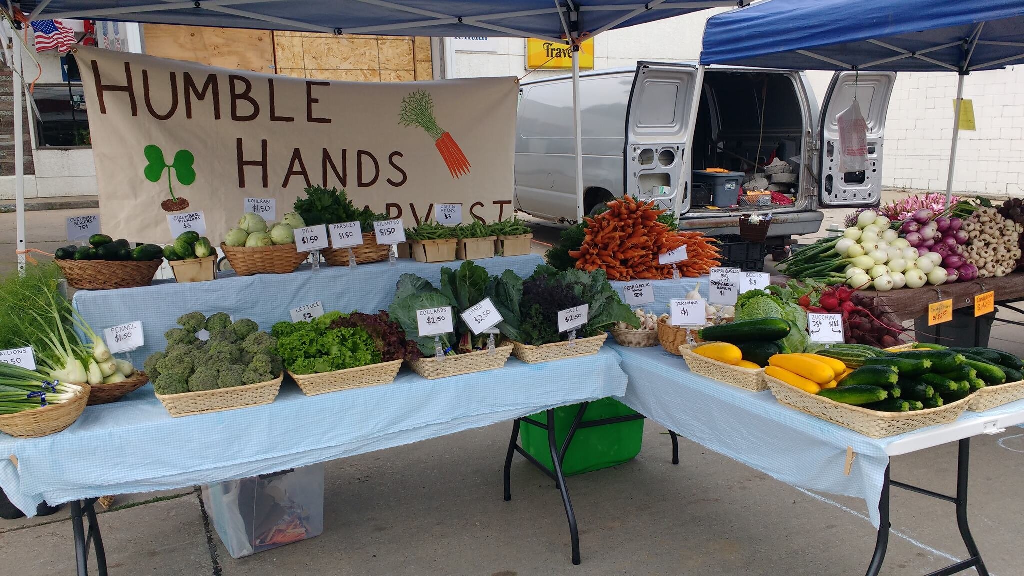 Tables at farmers market with Humble Hands Harvest sign