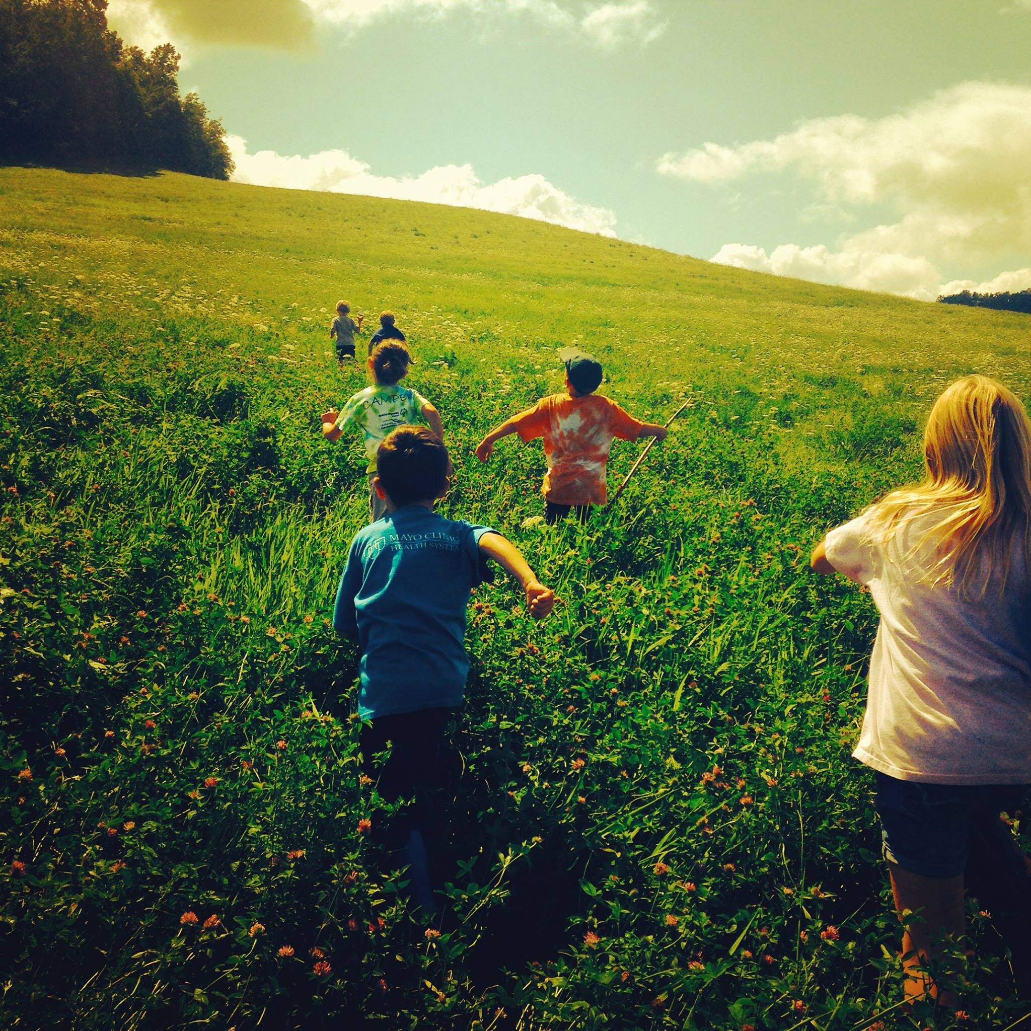 children running through sunny prairie field