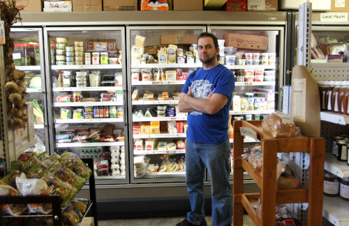 Store owner standing in front of a cooler full of dairy products