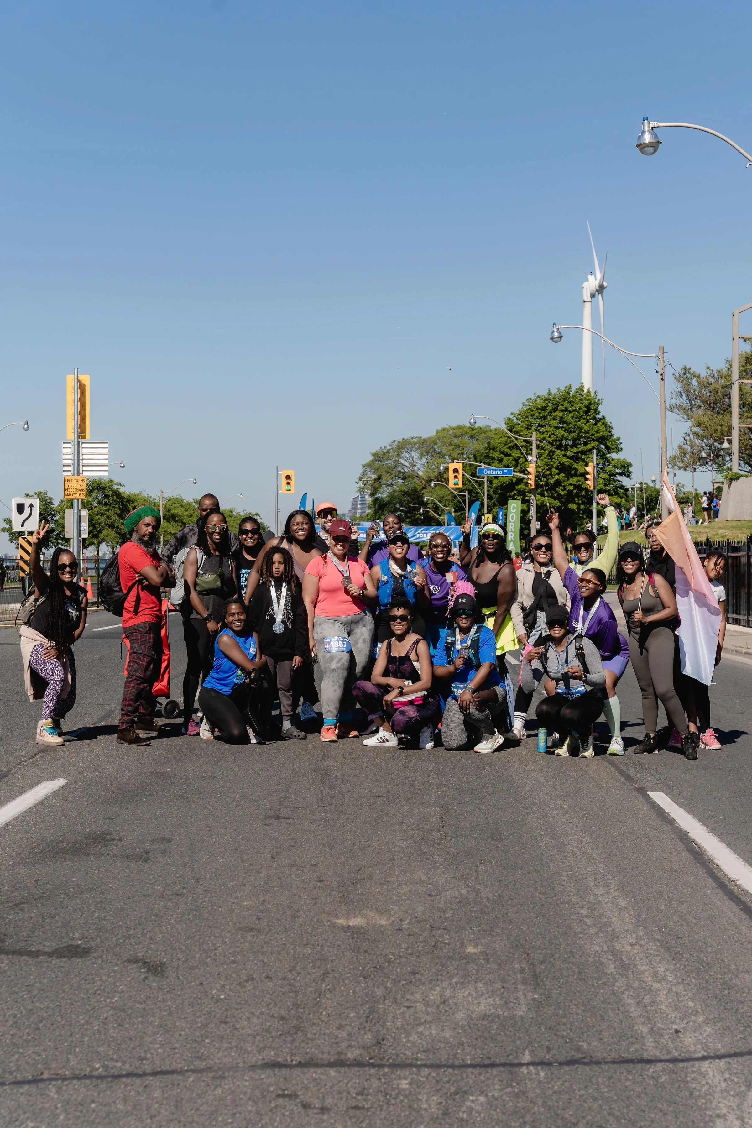 Group of people participating in a charity walk or run on a city street, wearing athletic clothing and medals, with some holding banners and flags.