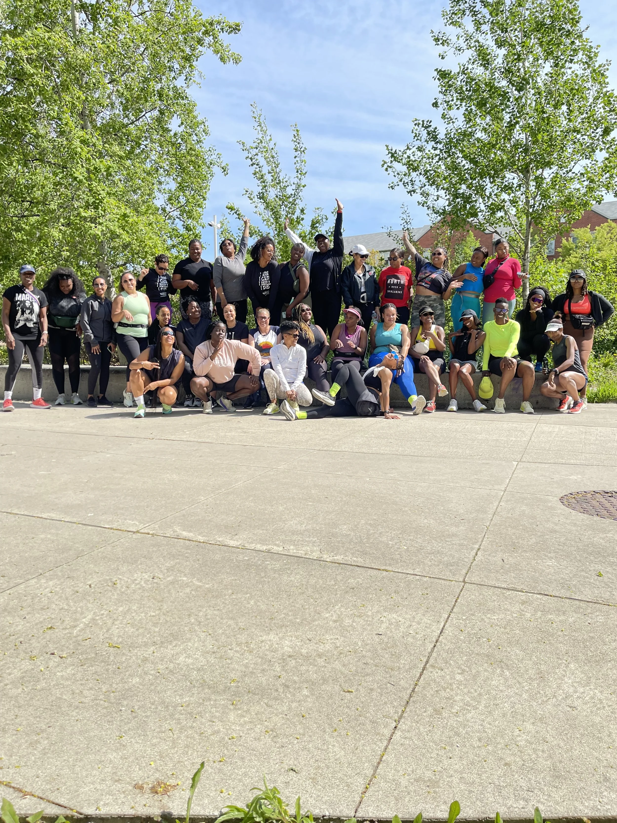 A group of diverse people posing outdoors on a sunny day with green trees in the background.