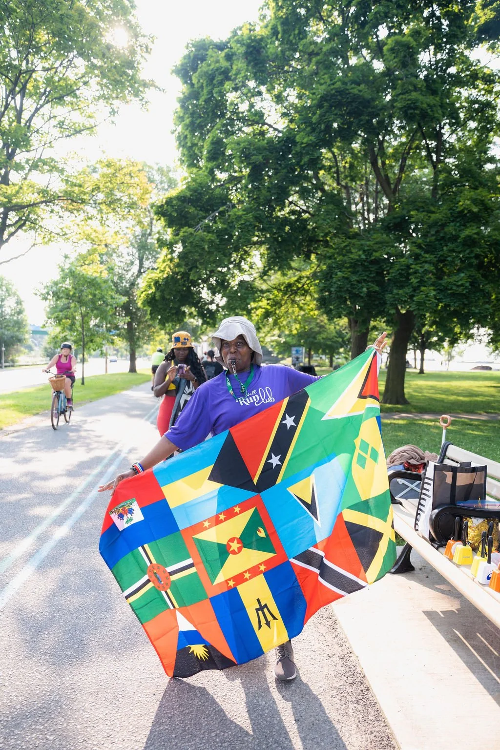 Person holding a colorful flag with flags from various Caribbean countries in a park on a sunny day.
