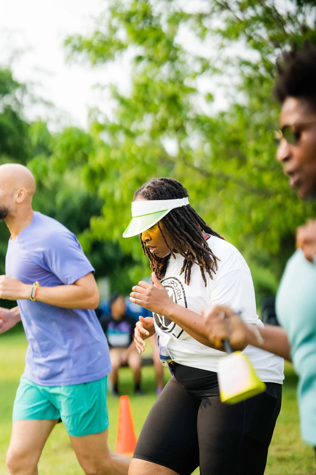 Group of people running outdoors during a sunny day, with green trees in the background.