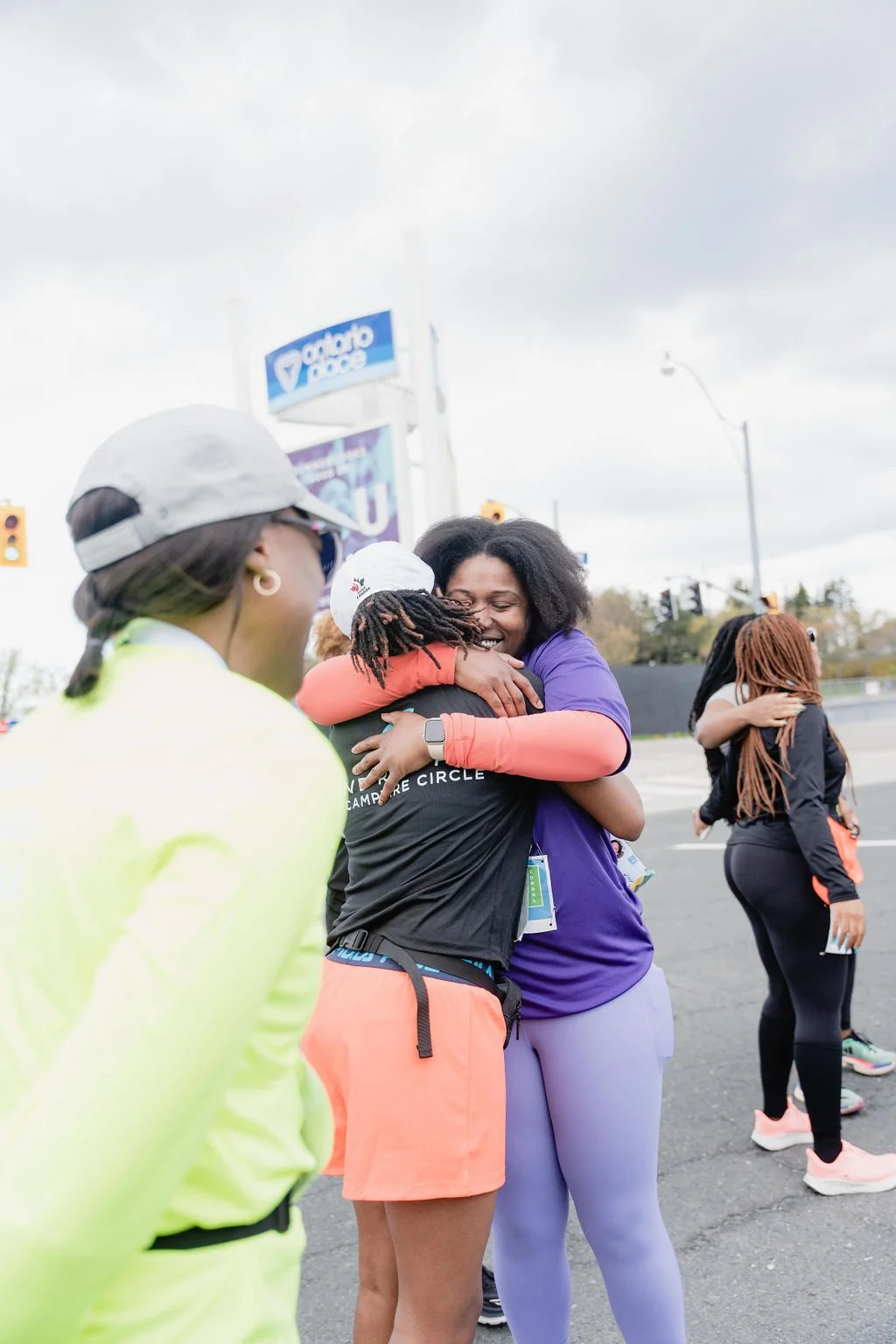 People hugging and smiling during a daytime event, with a woman wearing a purple shirt and others in athletic wear.