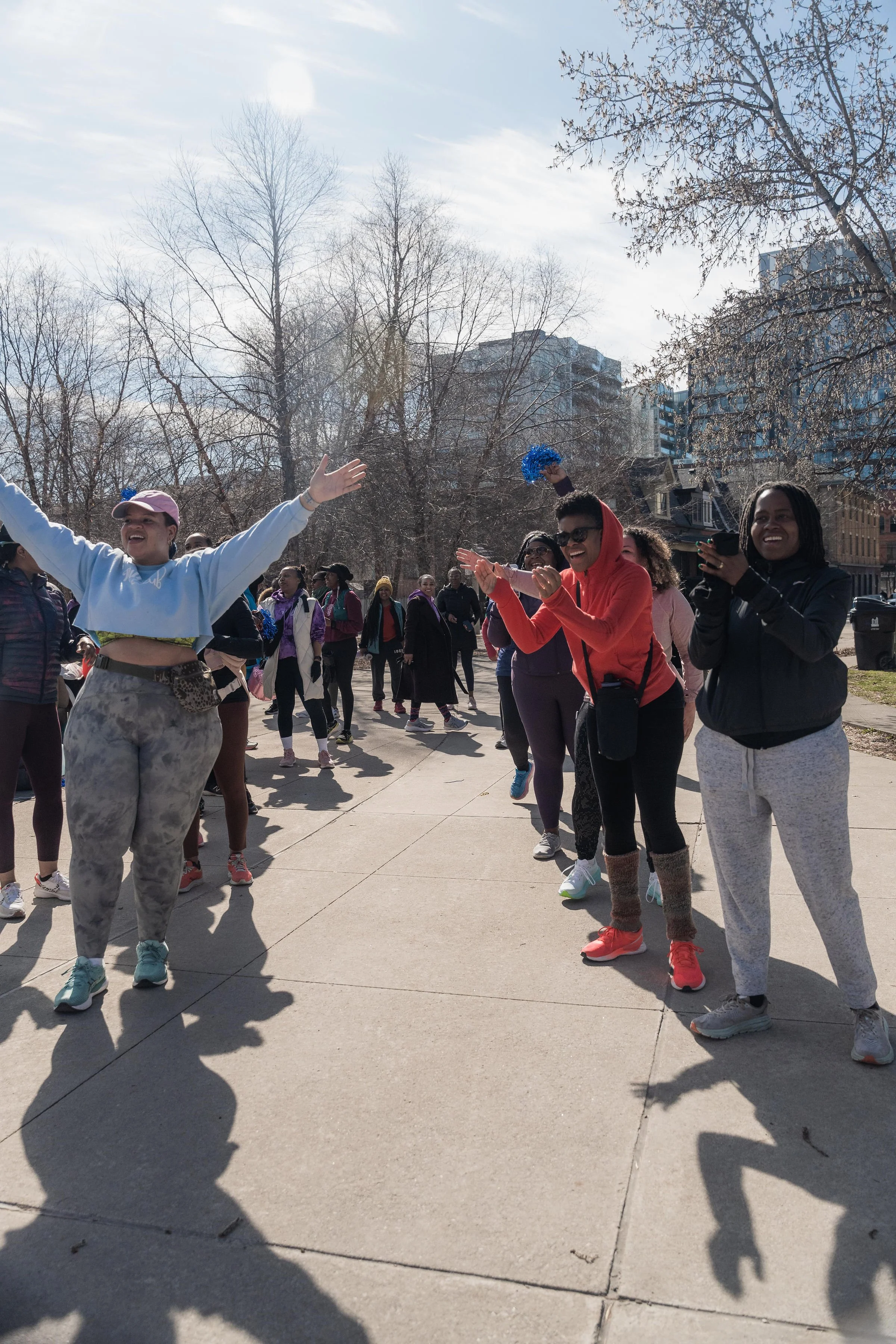 A group of women participating in an outdoor event or gathering in a park on a sunny day, with some clapping and smiling.