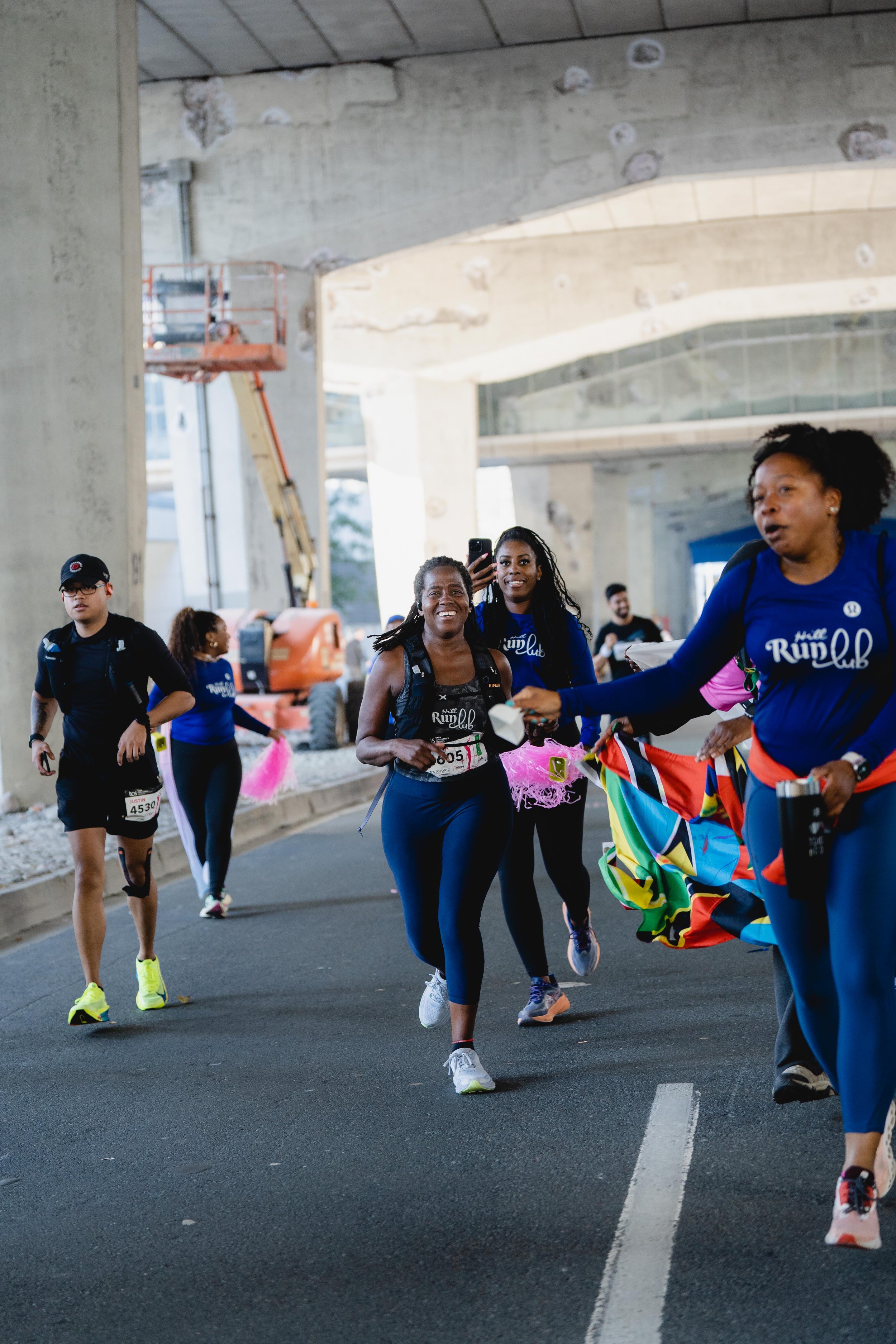 Group of runners participating in a marathon or race under a bridge, with one runner receiving a finishing medal or award.