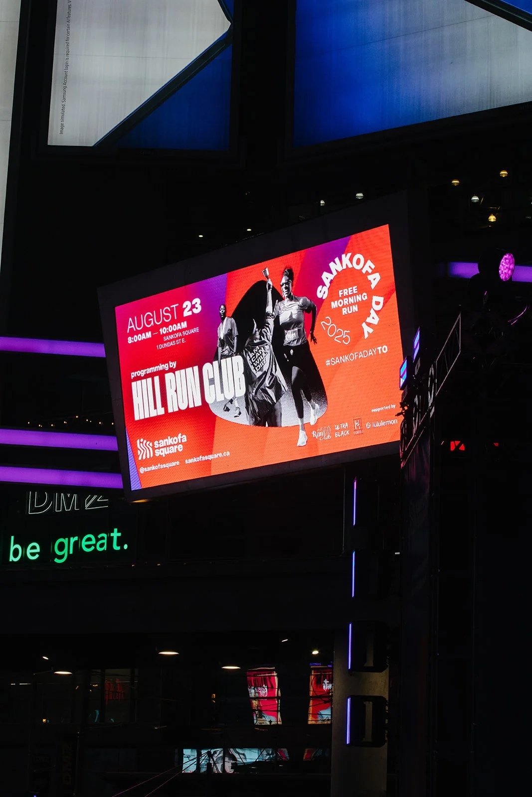 Digital billboard advertising a free morning run event called Sankofa Day 2025, scheduled for August 23 from 8:00 AM to 10:00 AM at Sankofa Square, with programming by Hill Run Club. The display features two women running and holding a trophy, with v