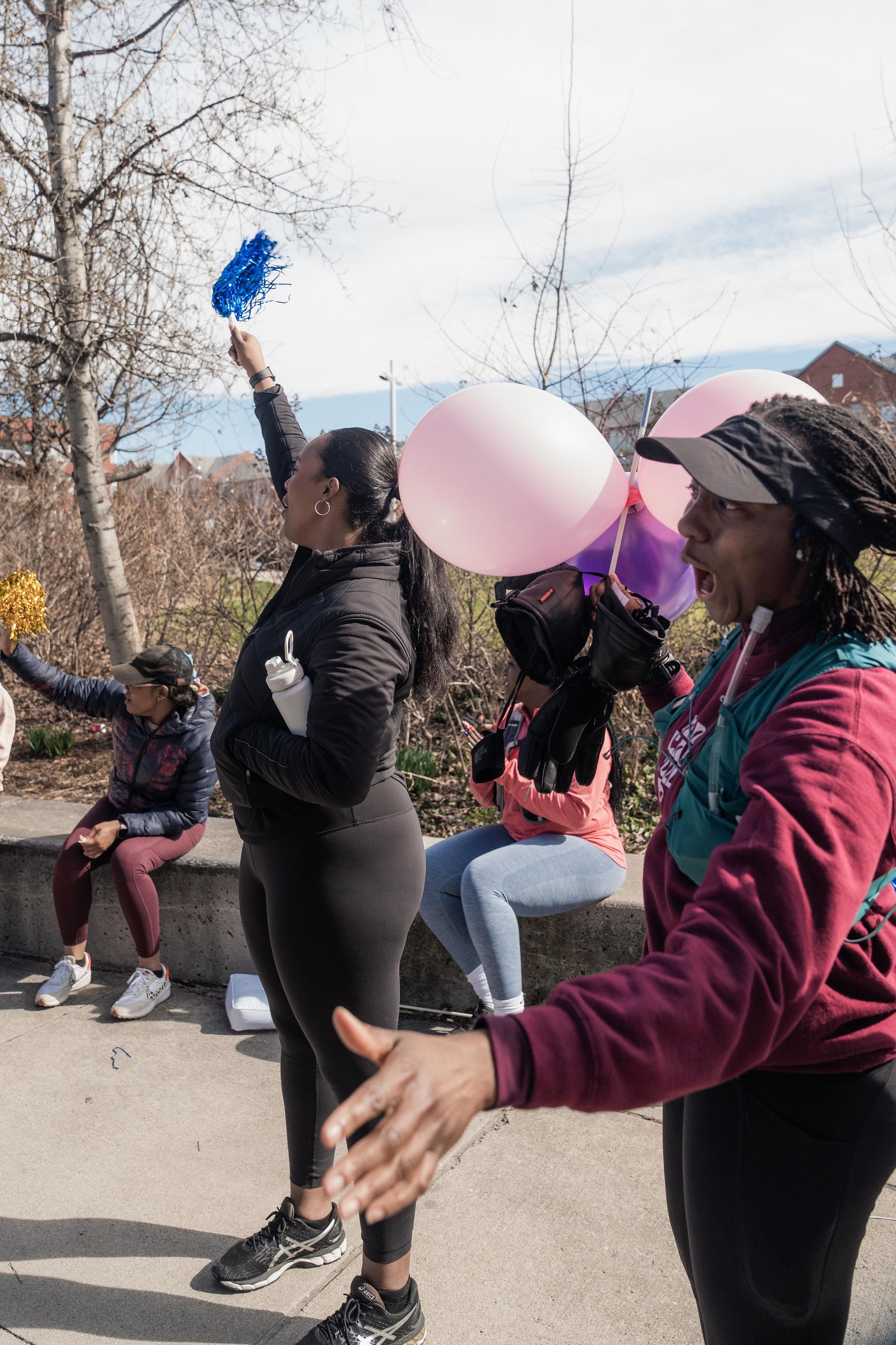 A group of people outdoors during daytime, with some holding balloons and others sitting on a ledge, participating in an event or celebration.