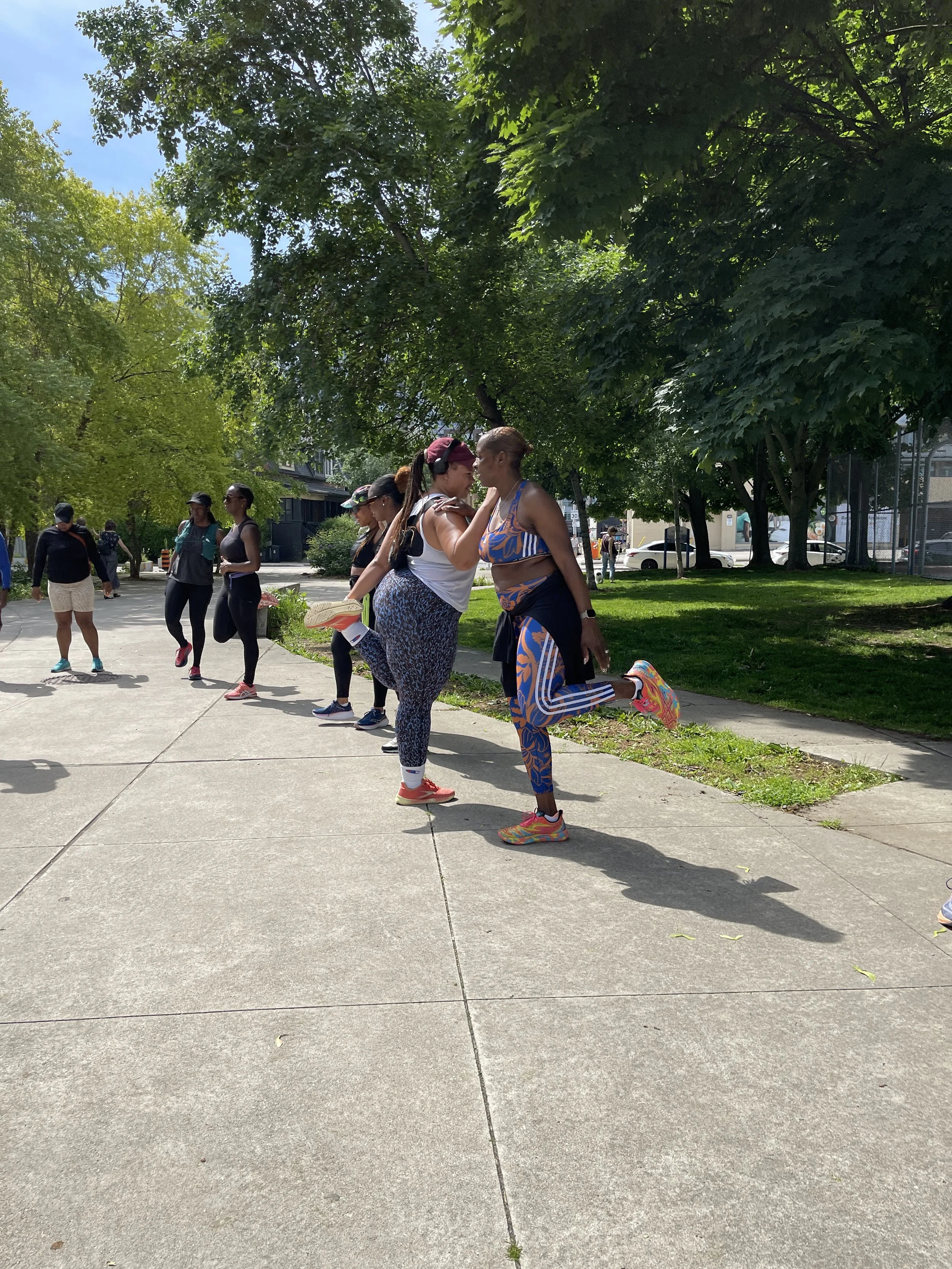 People participating in an outdoor fitness class in a park, stretching and engaging in warm-up exercises on a sunny day.