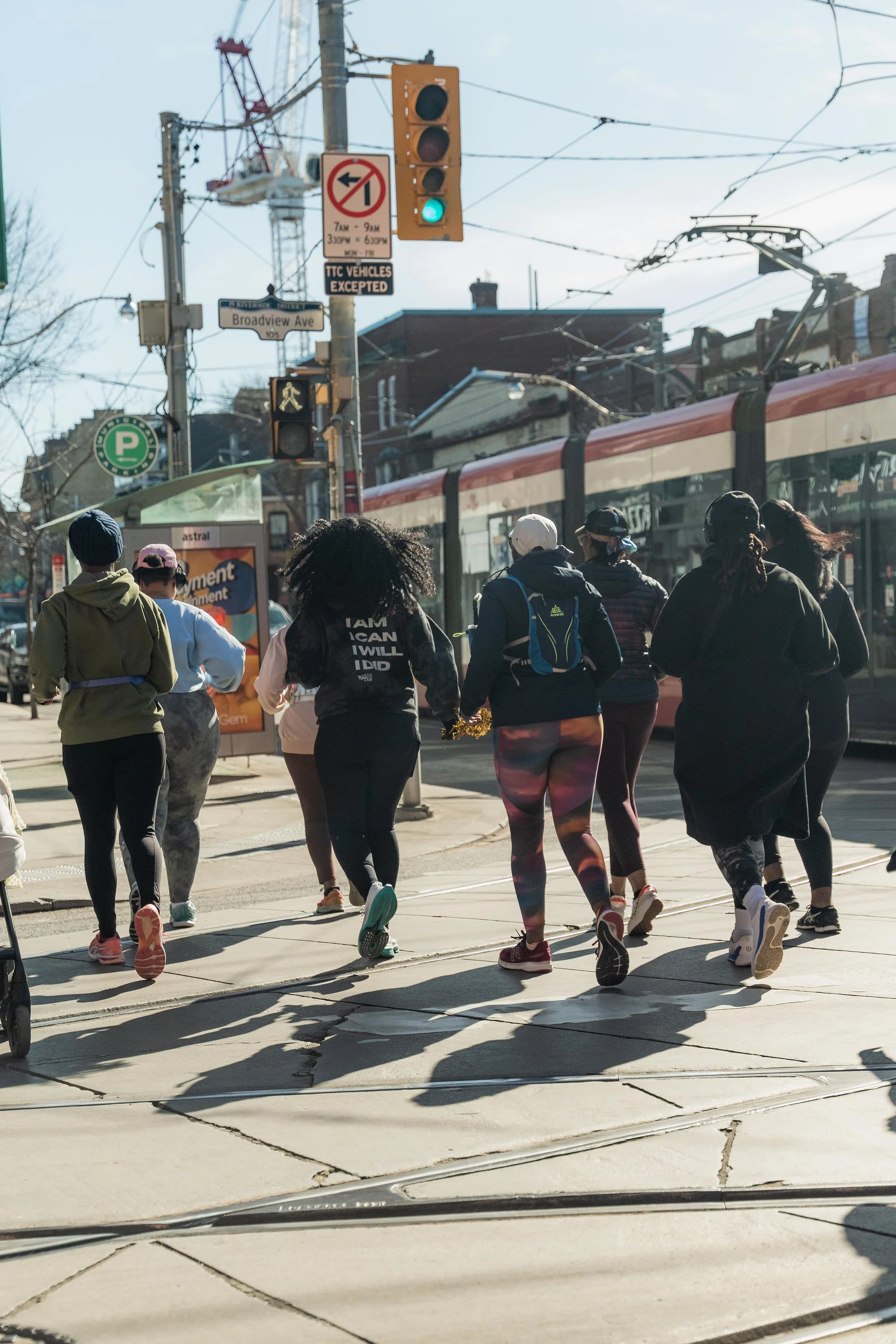 Group of people running across crosswalk in urban area with streetcar and traffic lights