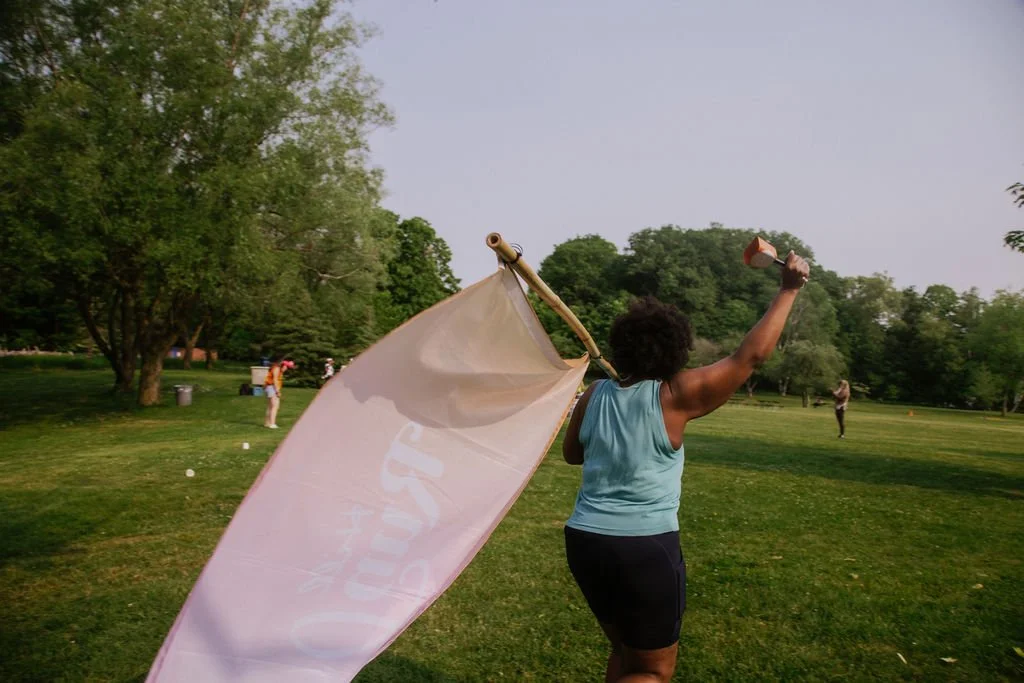 A person holding a large flag and a megaphone on a grassy park field with trees, during daytime.