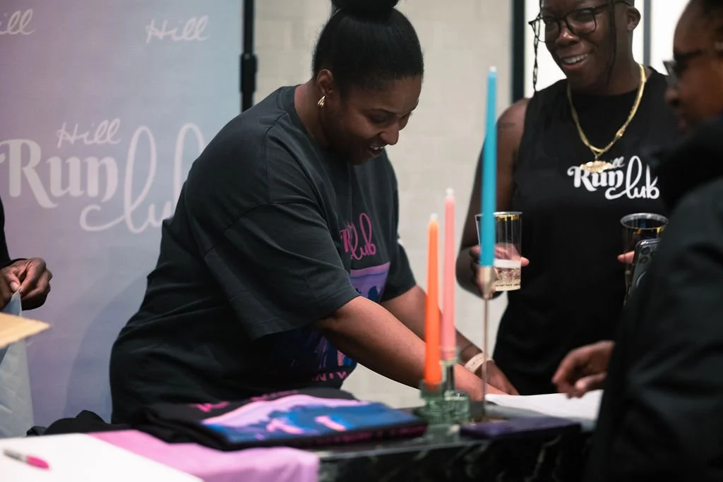 Women celebrating at a party with candles, drinks, and a wedding cake table.
