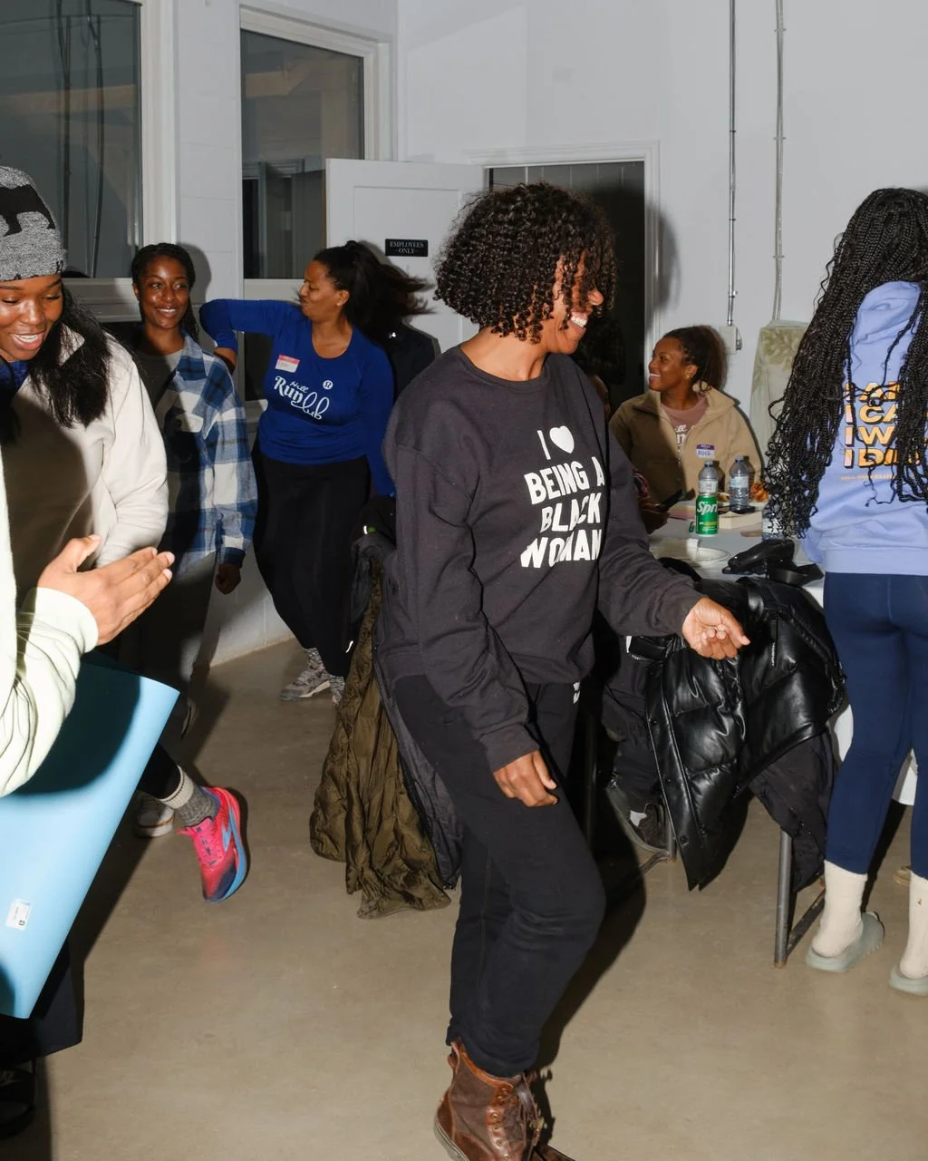 A group of women at an indoor gathering, laughing and talking, with some wearing shirts supporting causes related to Black women and empowerment.
