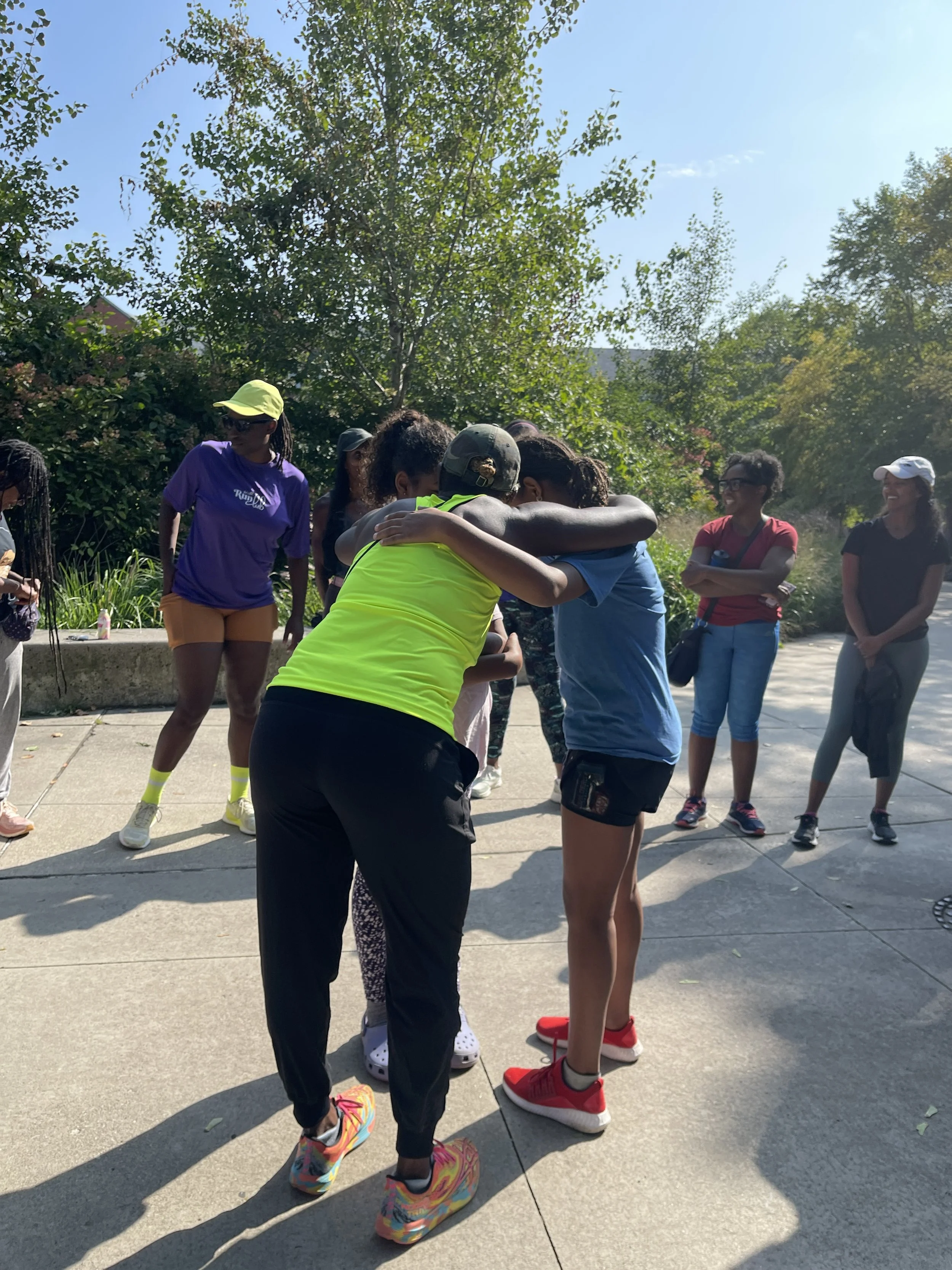 A group of women participating in an outdoor event, with two women hugging in the center, surrounded by others smiling and observing.