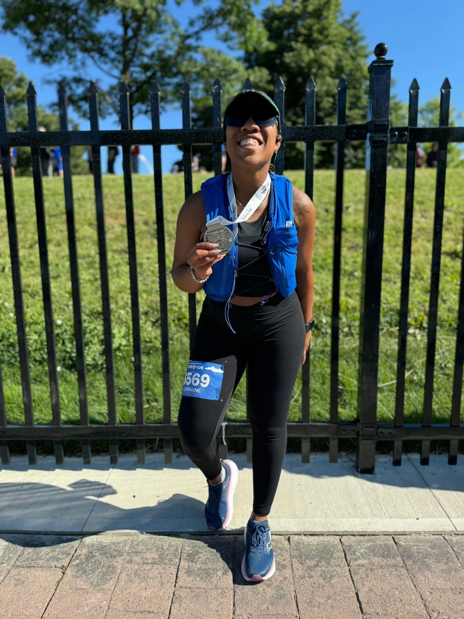 A woman in athletic gear holding a finisher medal, wearing a race bib with the number 1569, and smiling at a race event.