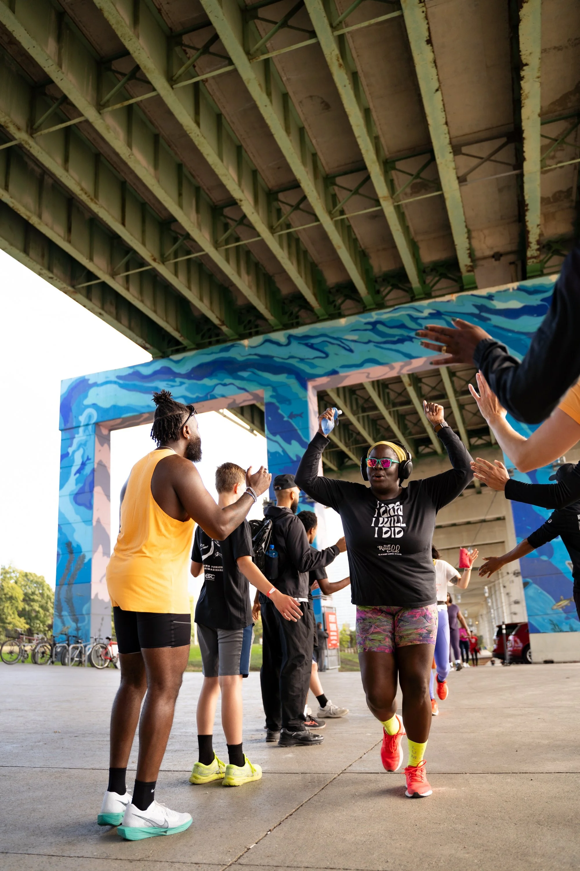 People celebrating at a marathon finish line under a bridge with colorful blue paint design.