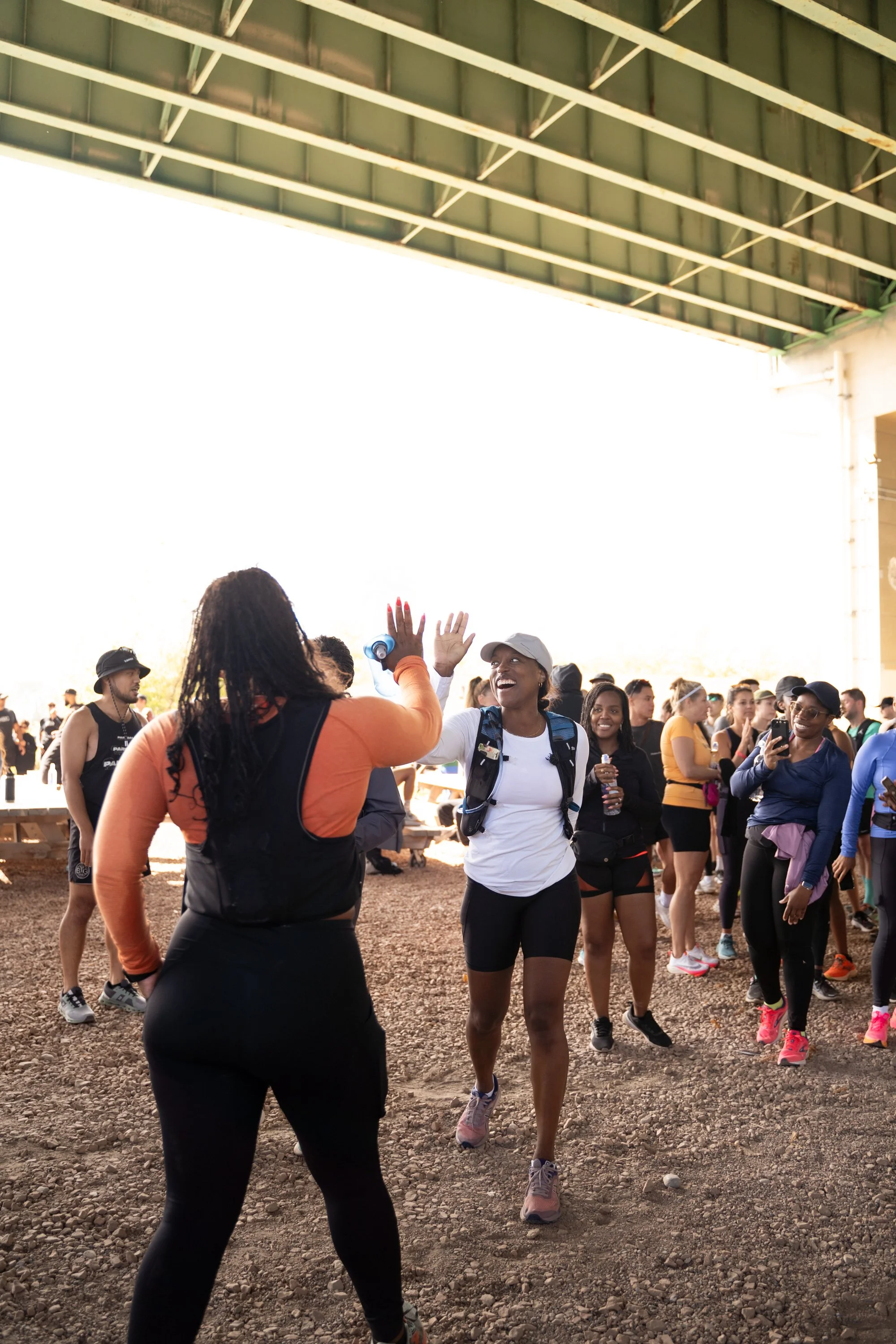 A group of people at an outdoor event are giving each other high fives and smiling under a large metal structure.