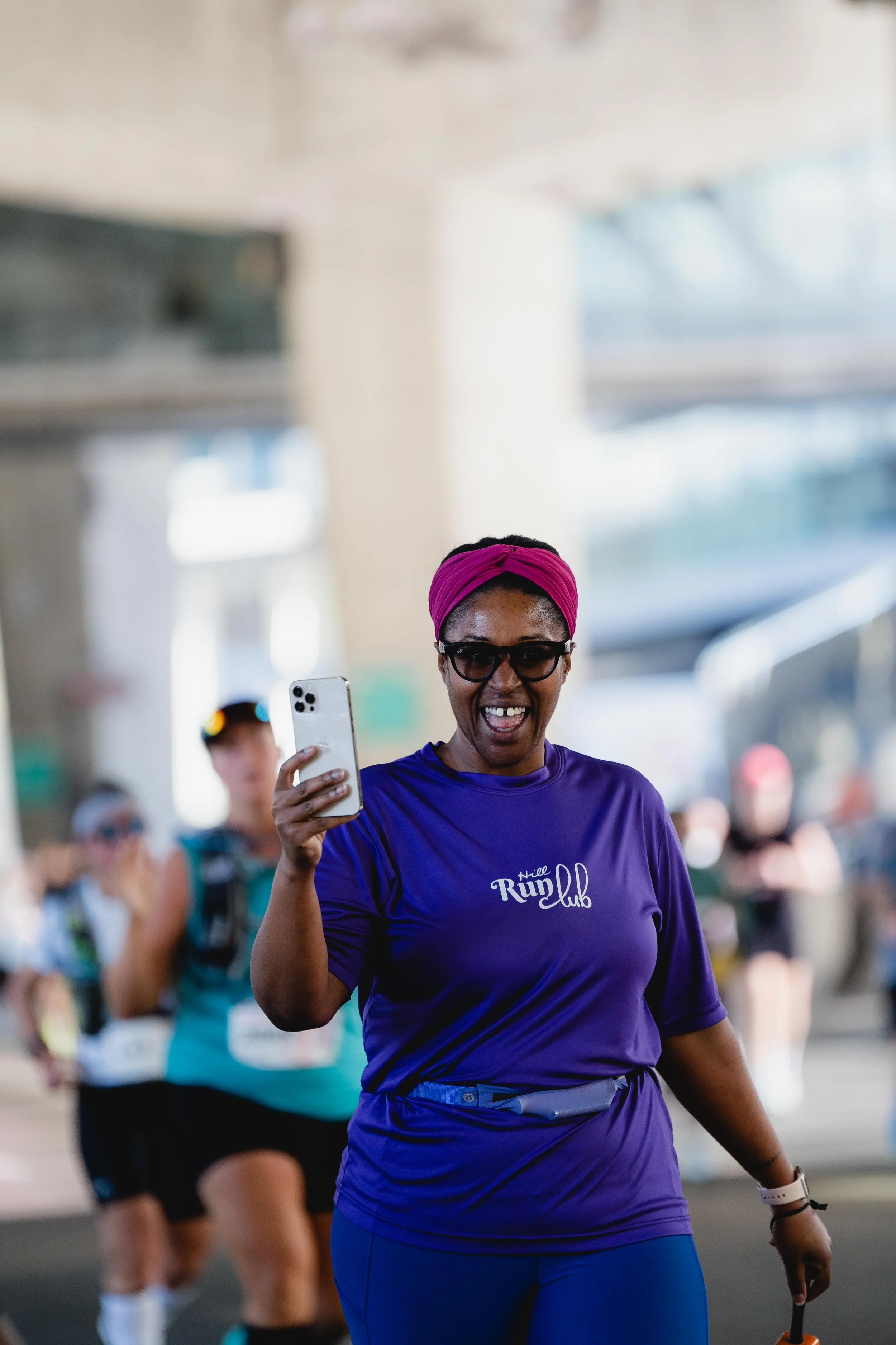 A woman in a purple athletic shirt and pink headband taking a selfie during a race.