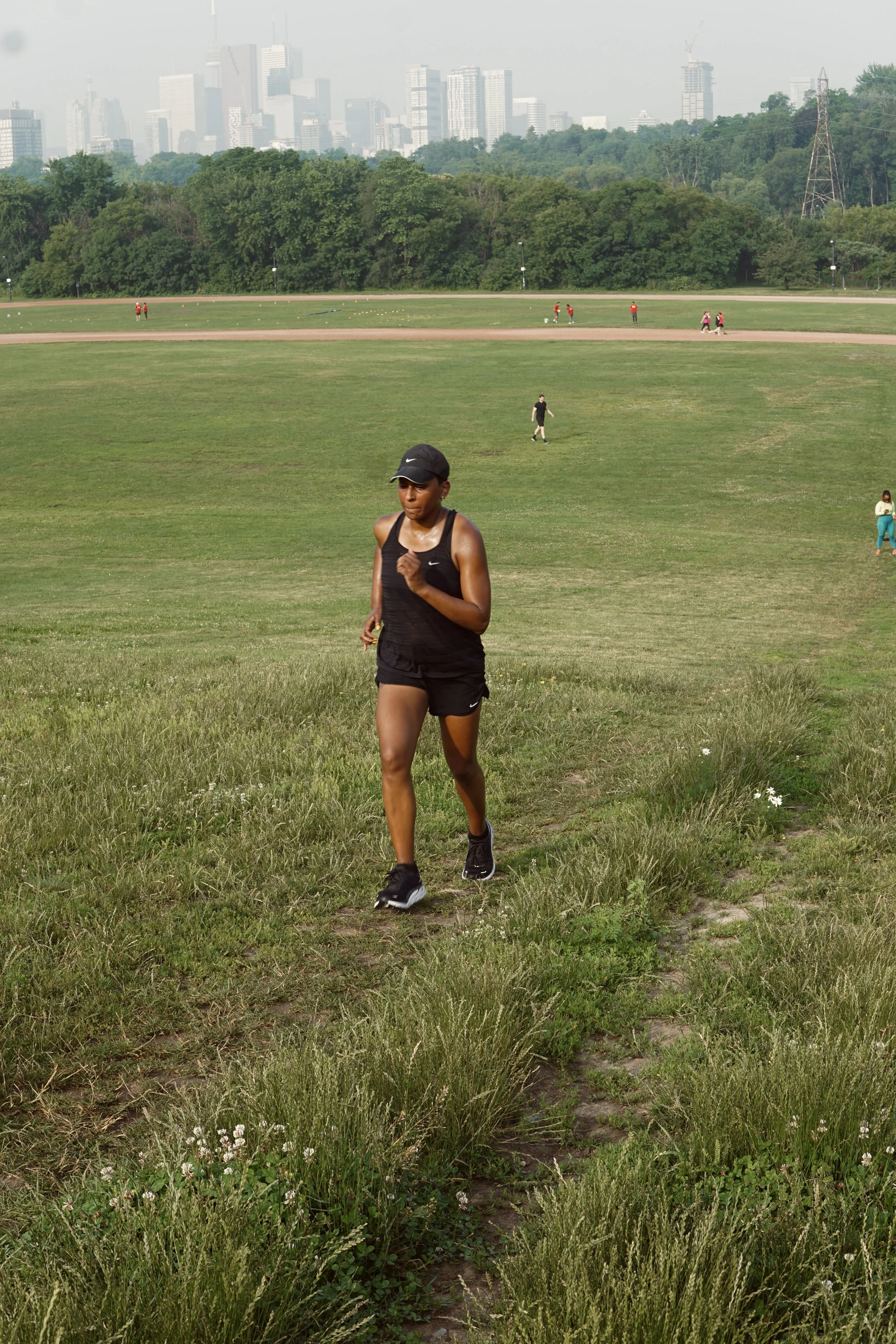 A woman jogging on a grassy trail in a park with a cityscape in the background.