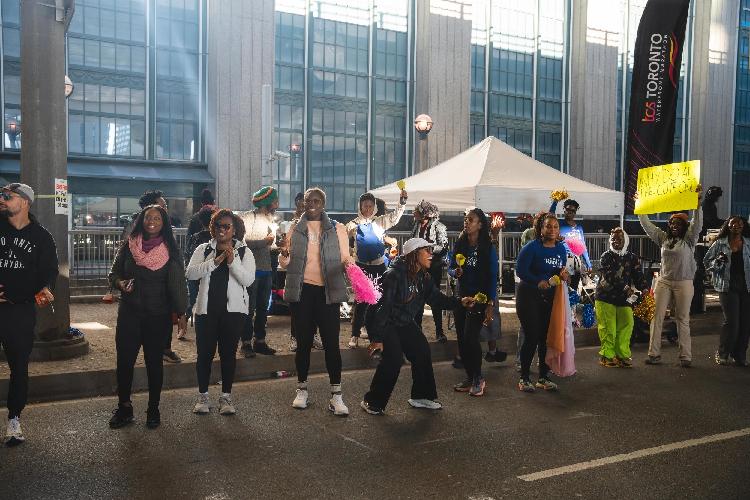A group of people gathered outdoors on a city street, holding signs and glow sticks, possibly participating in a protest or rally. There is a white tent and a banner in the background.