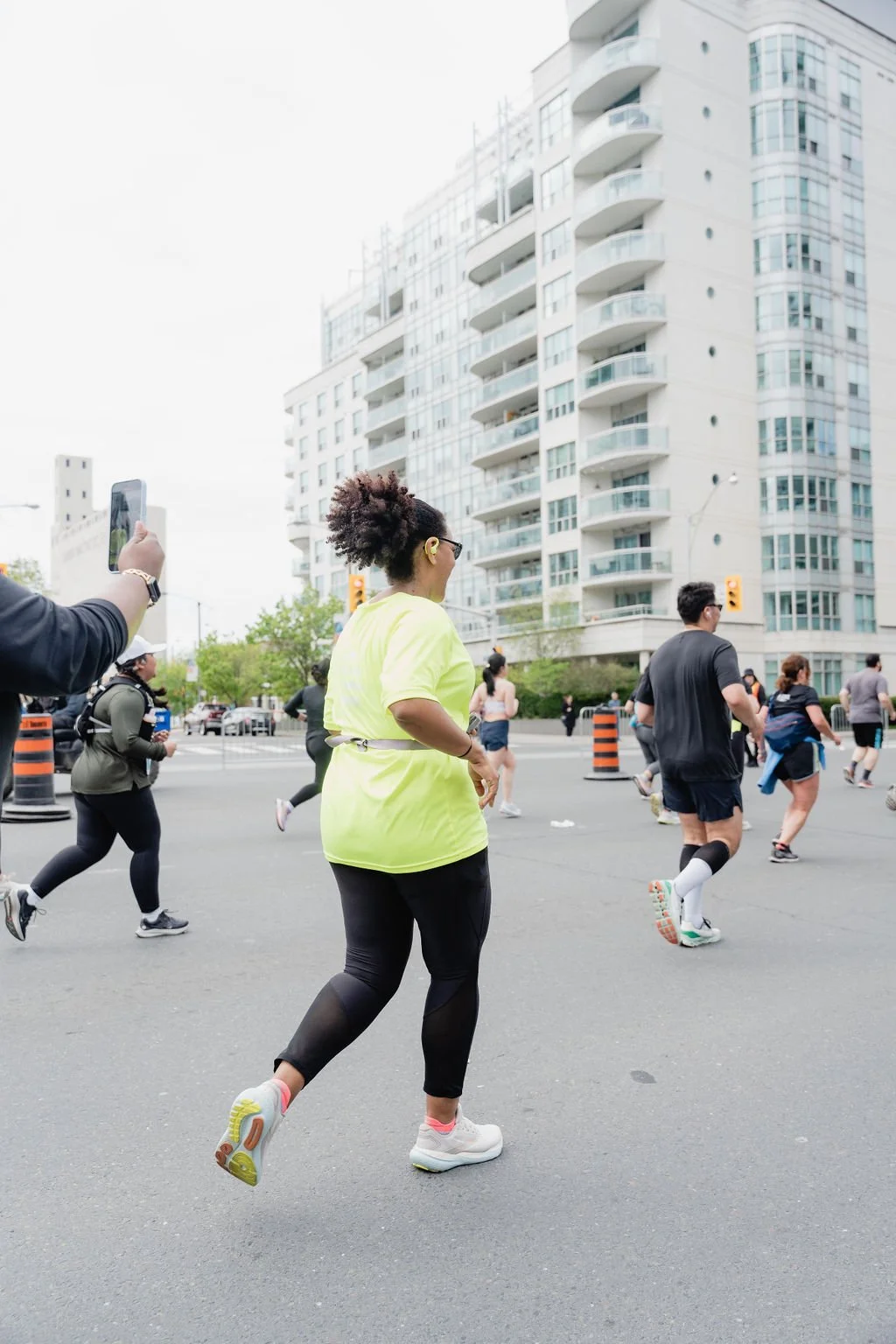 People participating in a city race or marathon, running on a city street with tall buildings in the background.