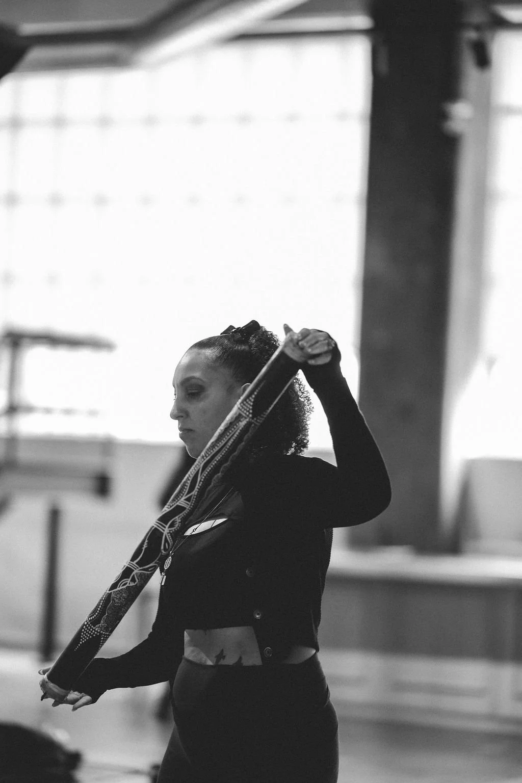 A woman with curly hair is adjusting a tennis racquet in a gym or sports facility.