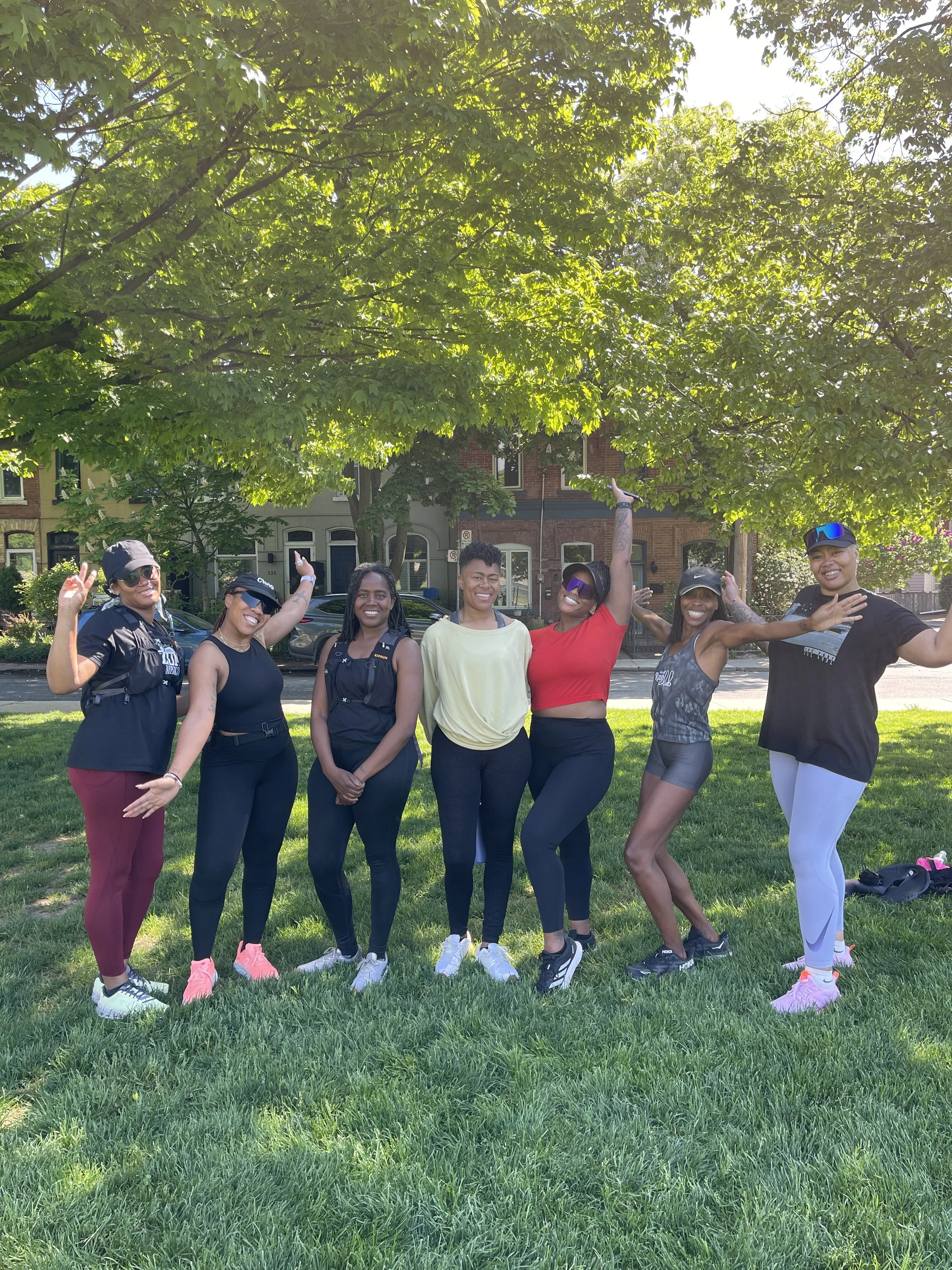 Group of seven women standing on grass under tree, smiling and posing for the photo.