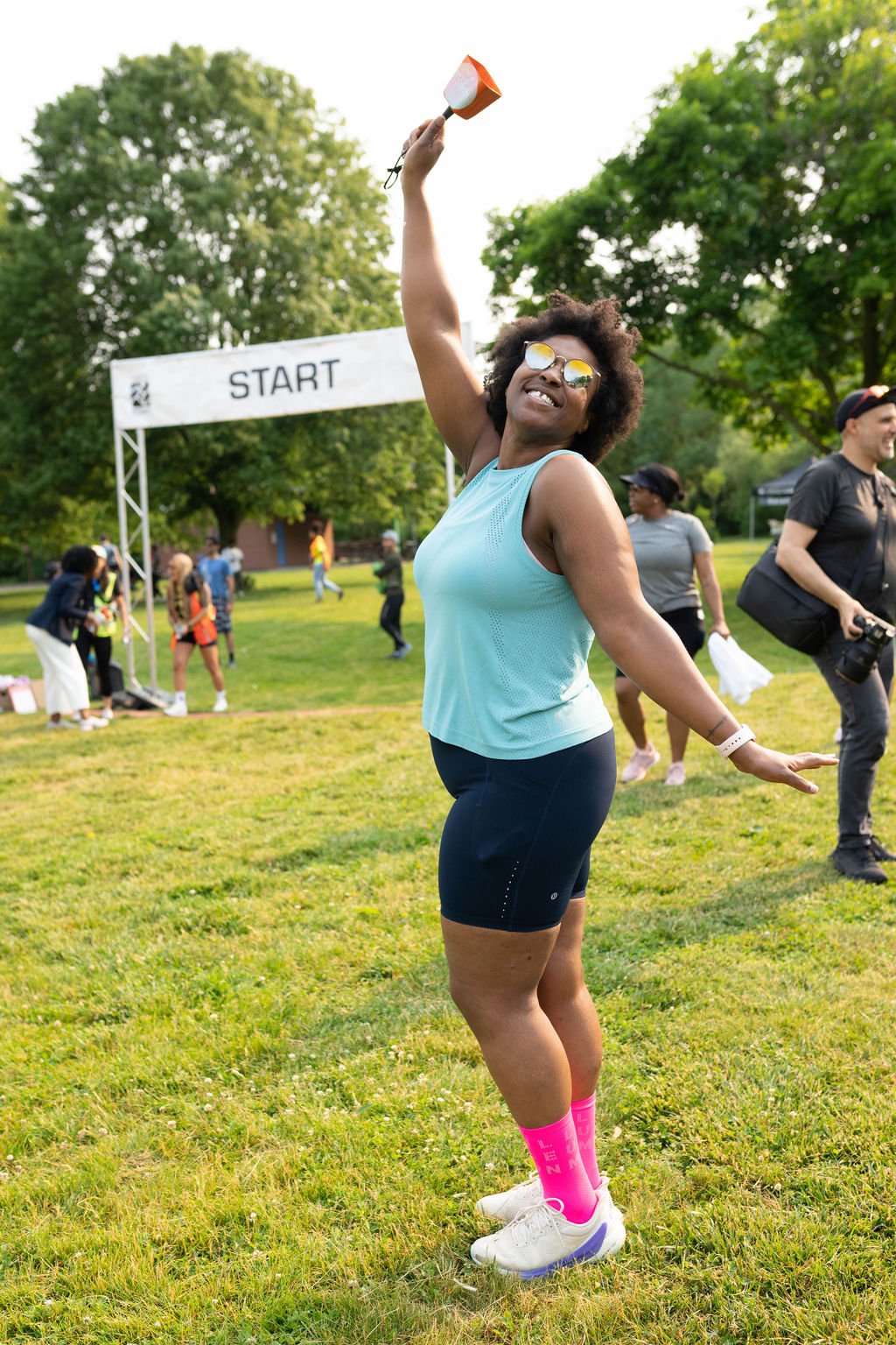 Woman in athletic clothing celebrating at a park starting line during a race event.