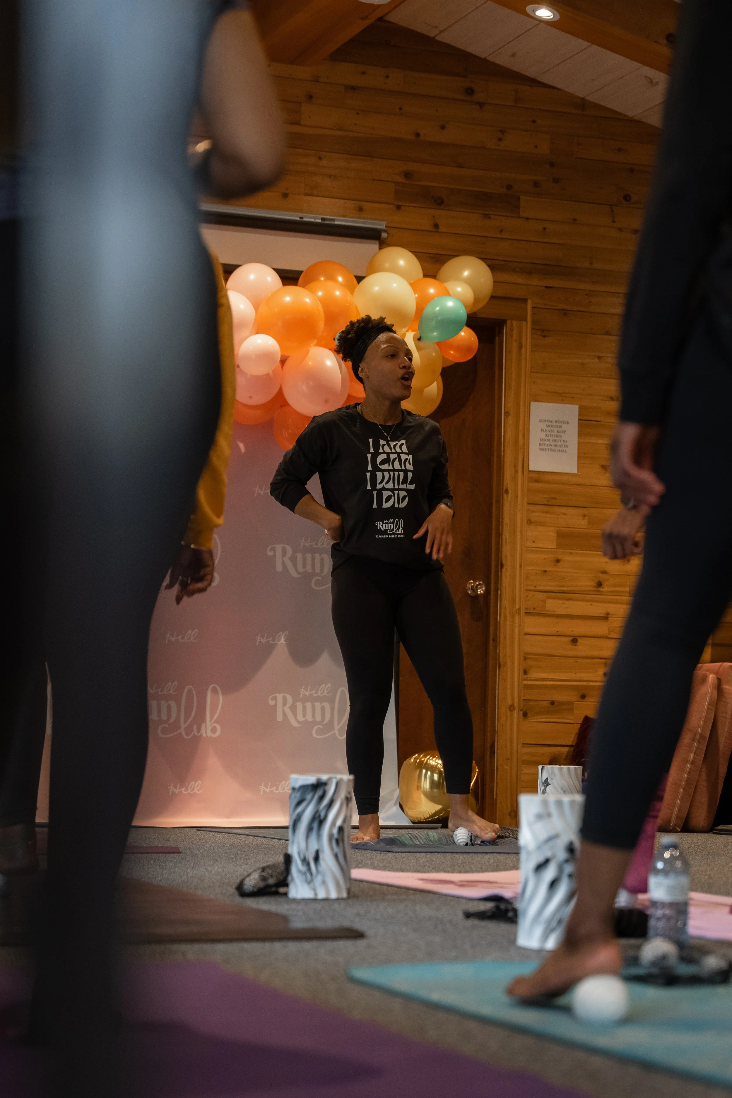 A woman leading a yoga class in a wooden indoor studio with balloons in the background.