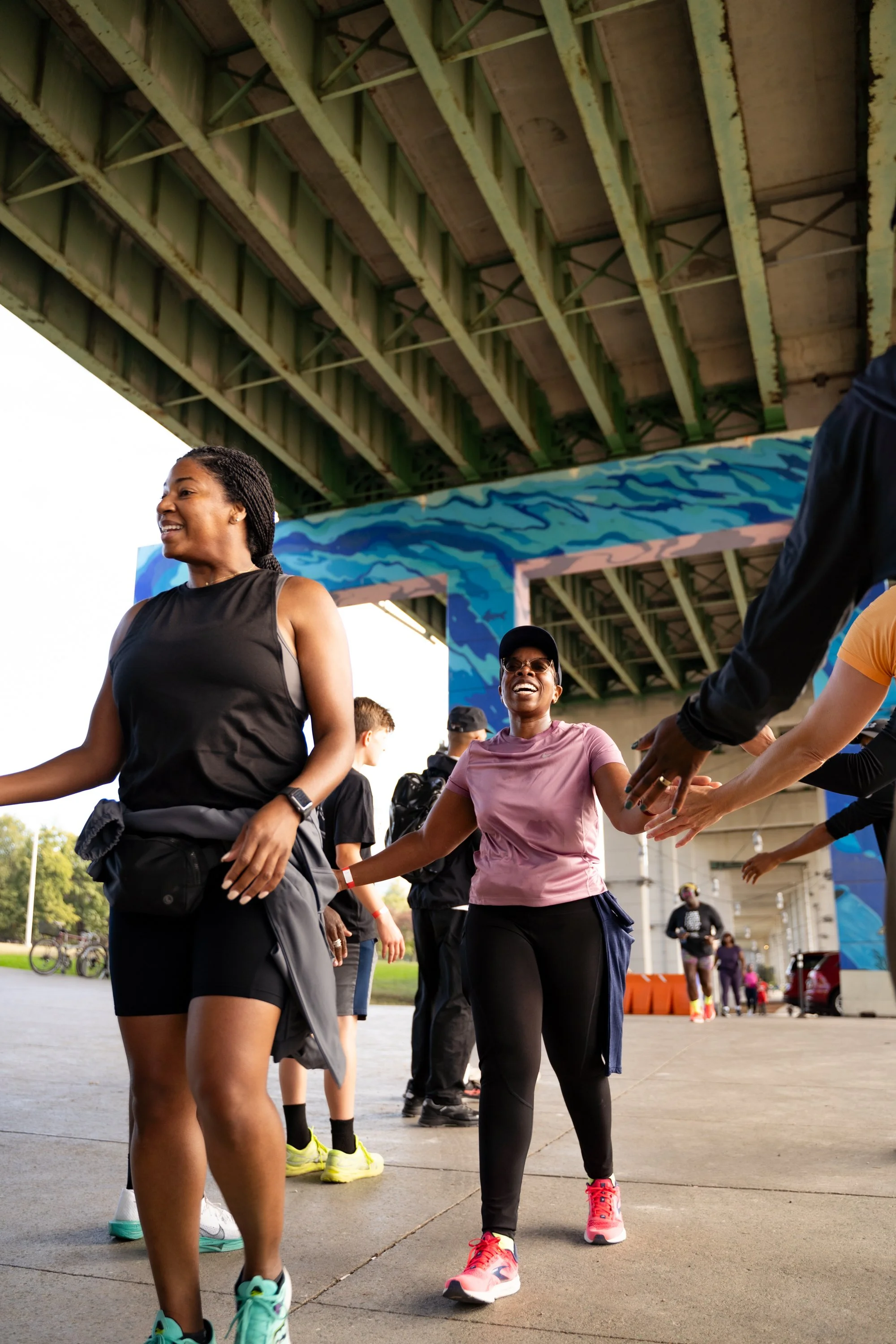 People under a bridge participating in a group activity, some smiling and reaching out to high-five or hold hands.
