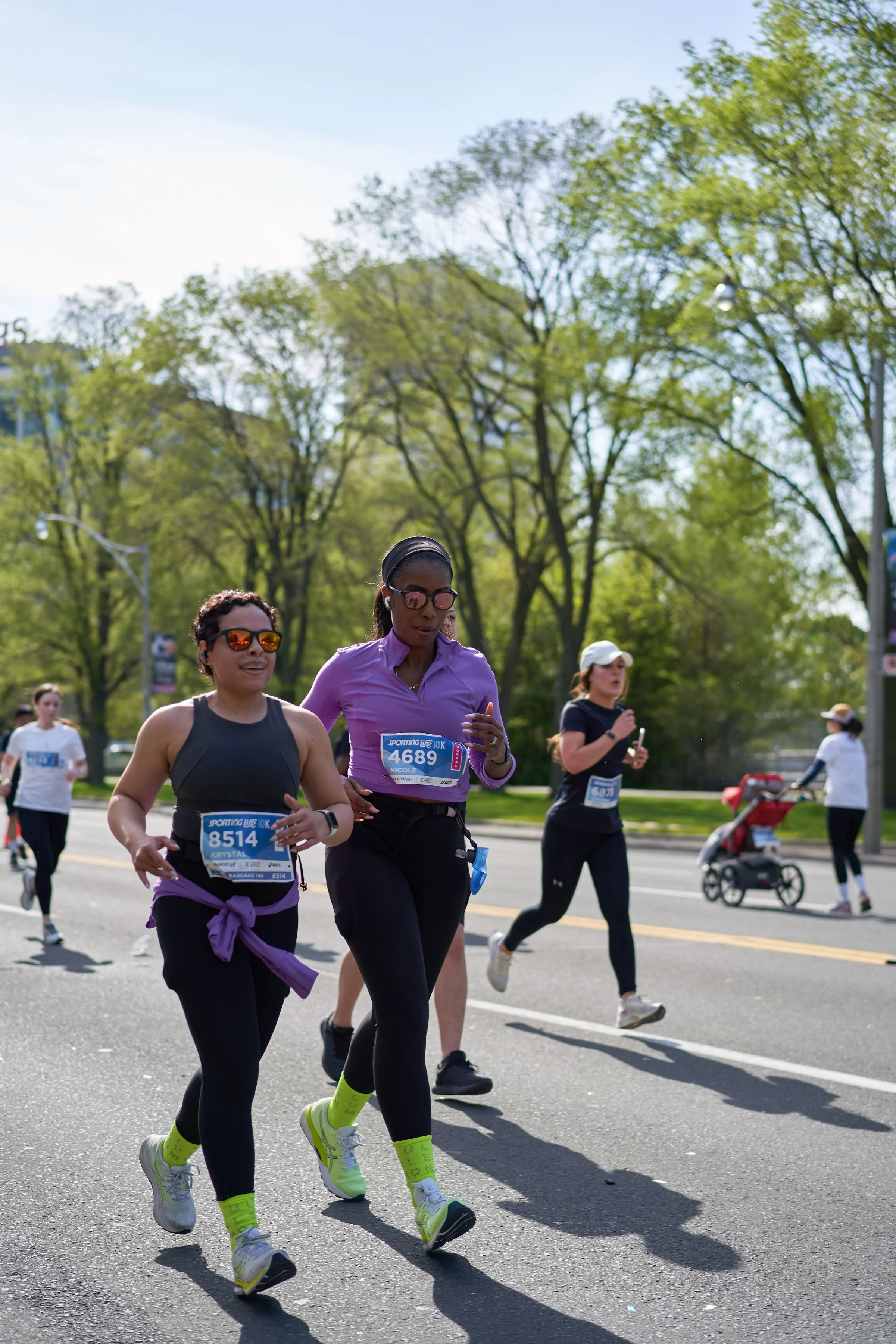 Black runners participating in Sporting Life 10K on a sunny day, with trees and street in the background.