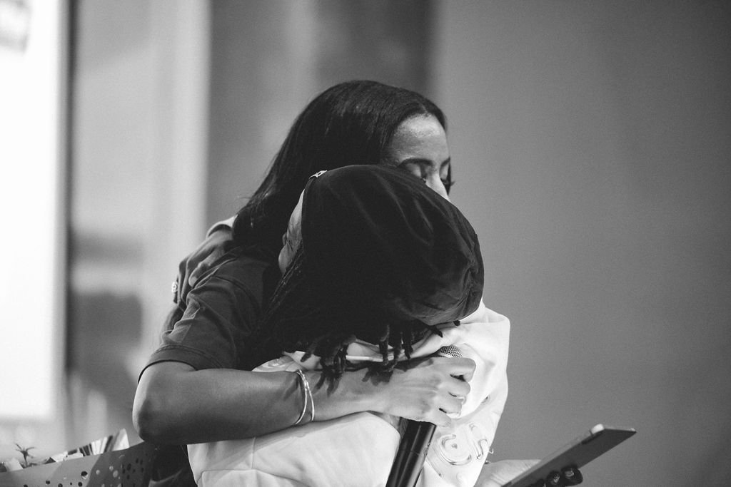 Two women hugging, one holding a microphone, in an emotional moment.