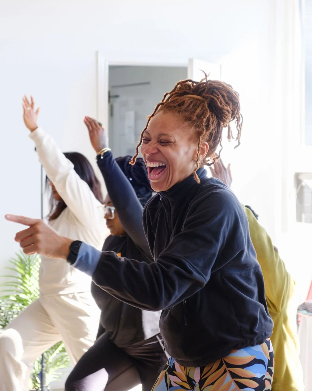 Woman with dreadlocks dancing and laughing with a group of people in indoor setting.