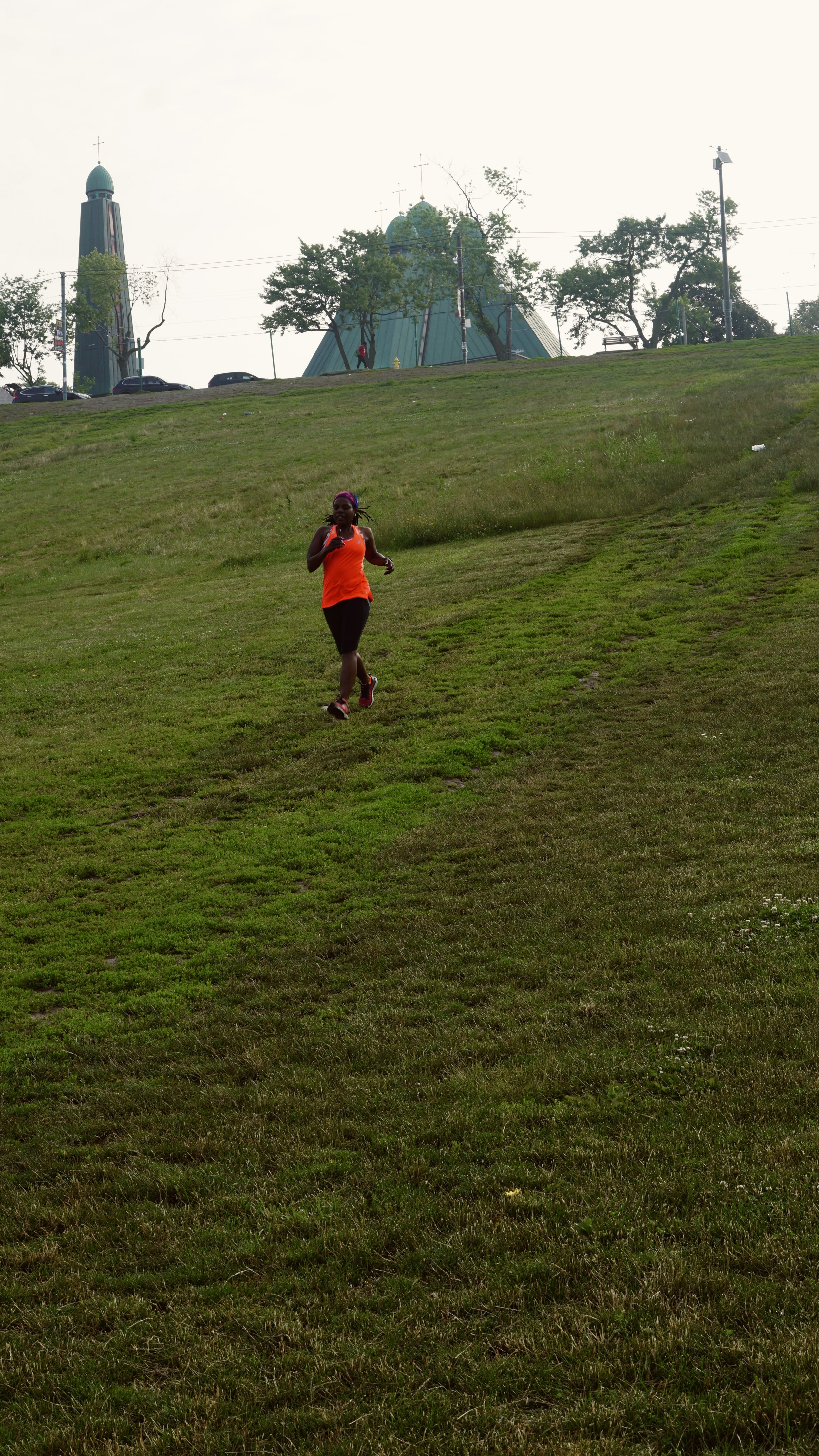 A woman jogging uphill on a grassy hill with a church in the background.