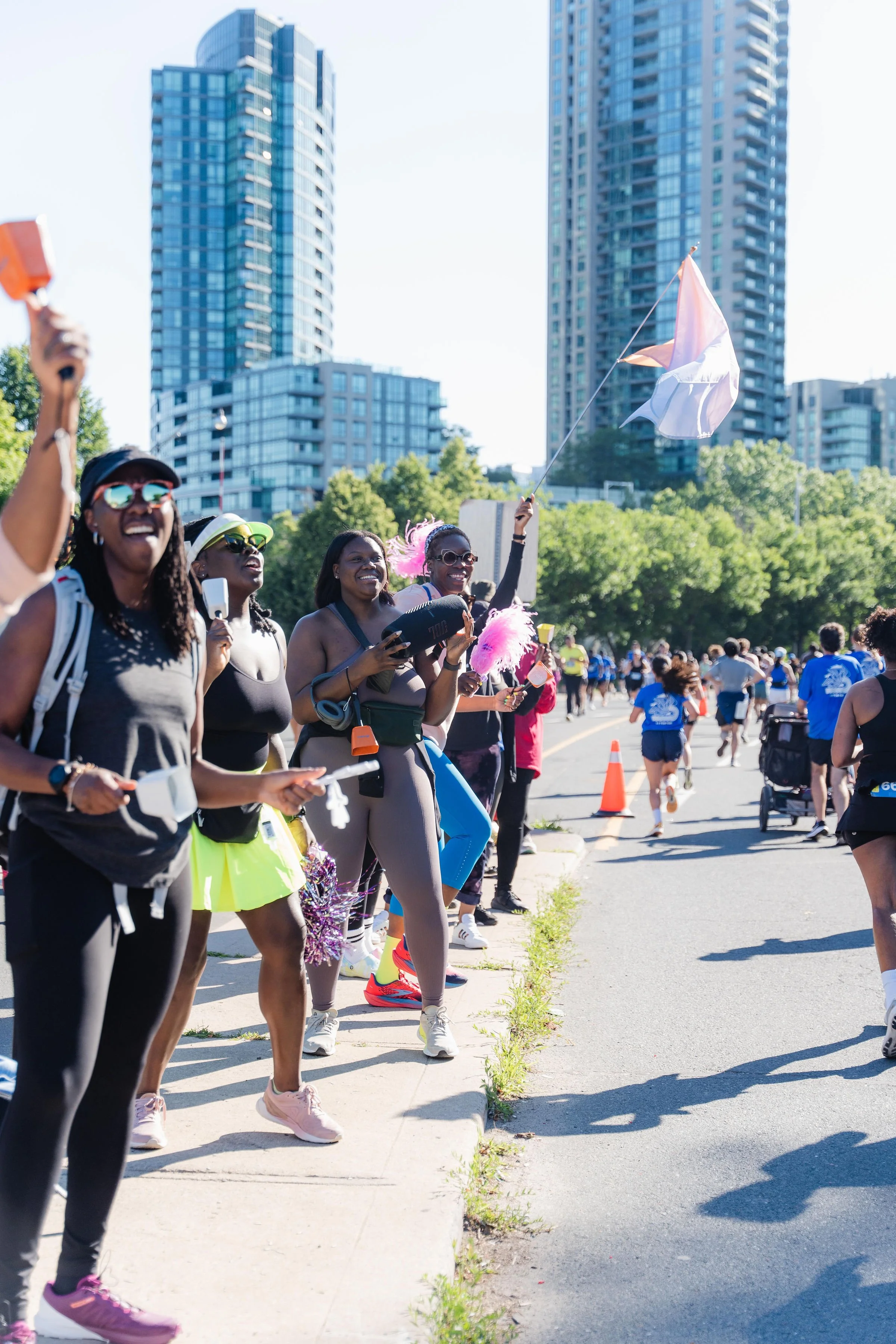 People participating in a marathon or outdoor race on a city street with high-rise buildings in the background, some smiling and cheering.