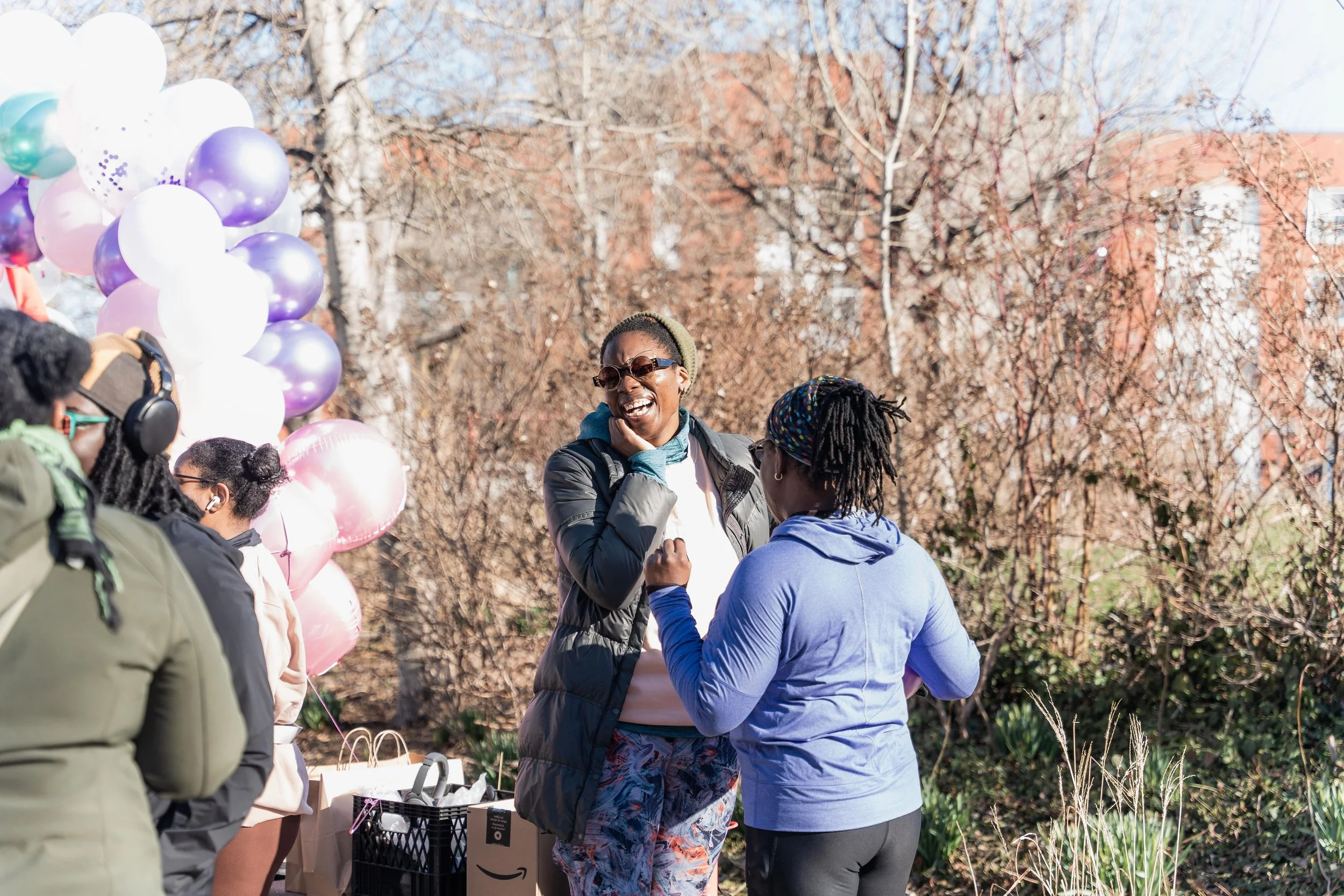 People talking and laughing outdoors during a daytime event, with balloons in the background.