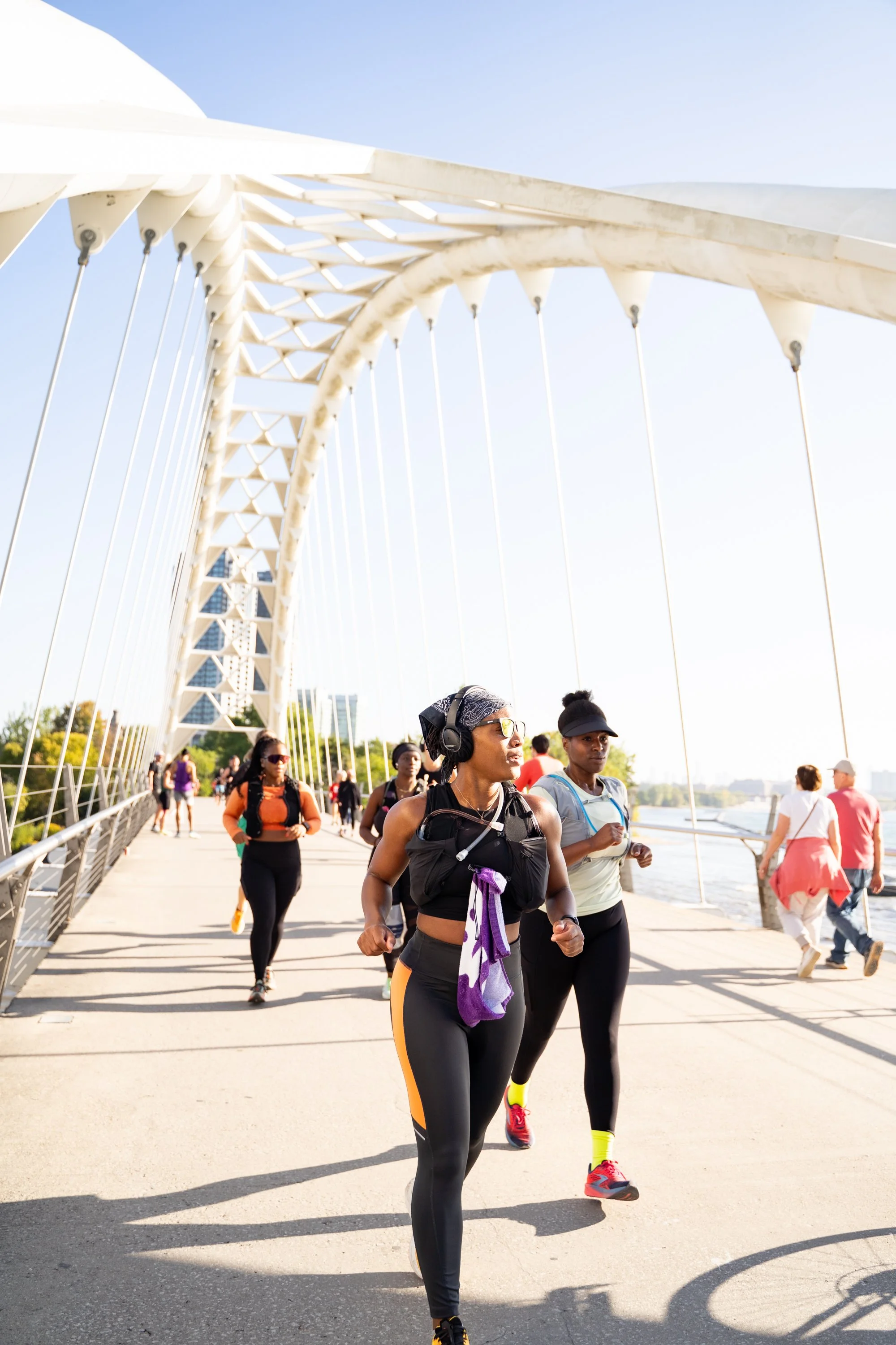 Black Women from Hill Run Club running across the Humber River bridge in Toronto near a body of water.
