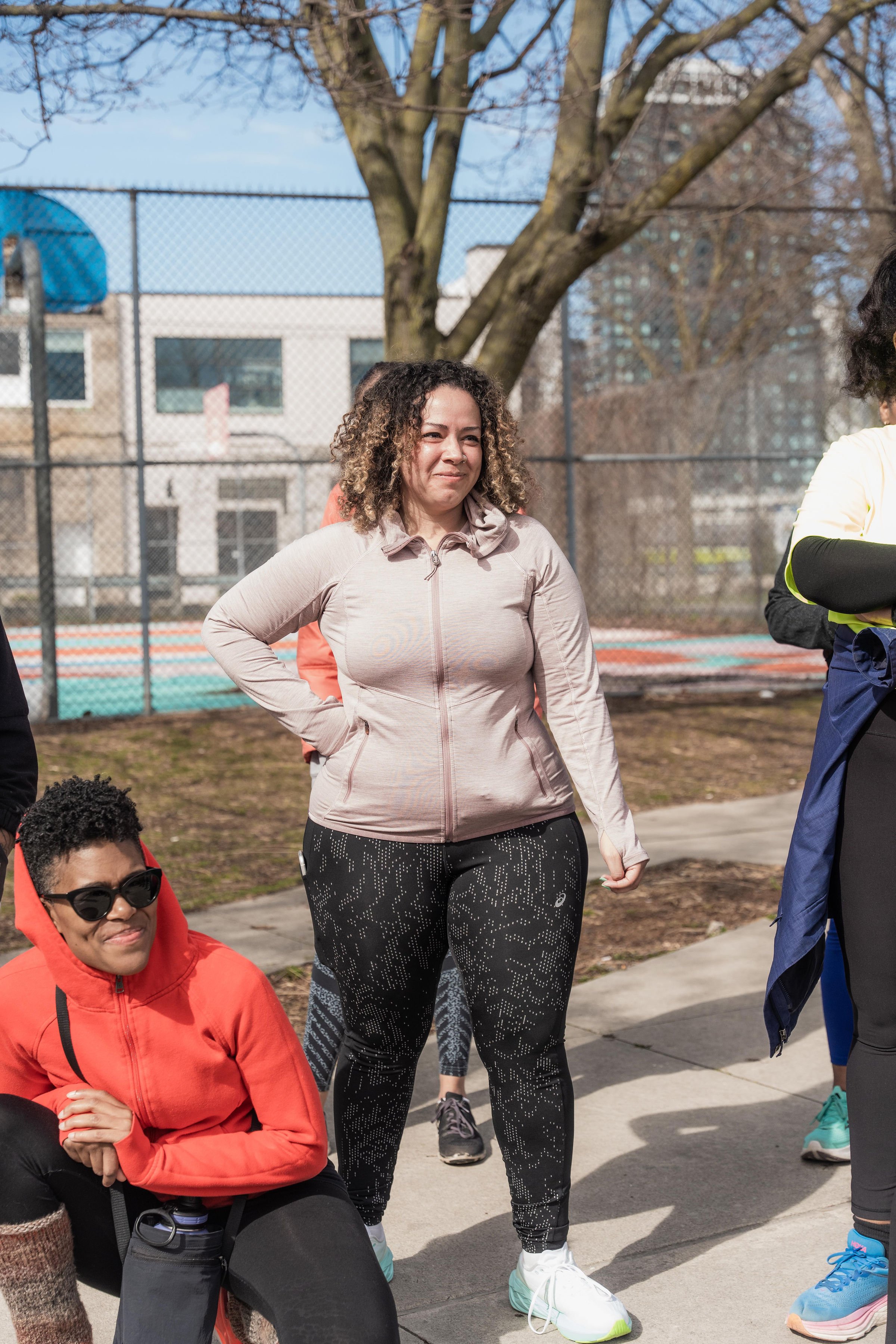 Group of diverse women in athletic gear standing outdoors near a tennis court on a sunny day.