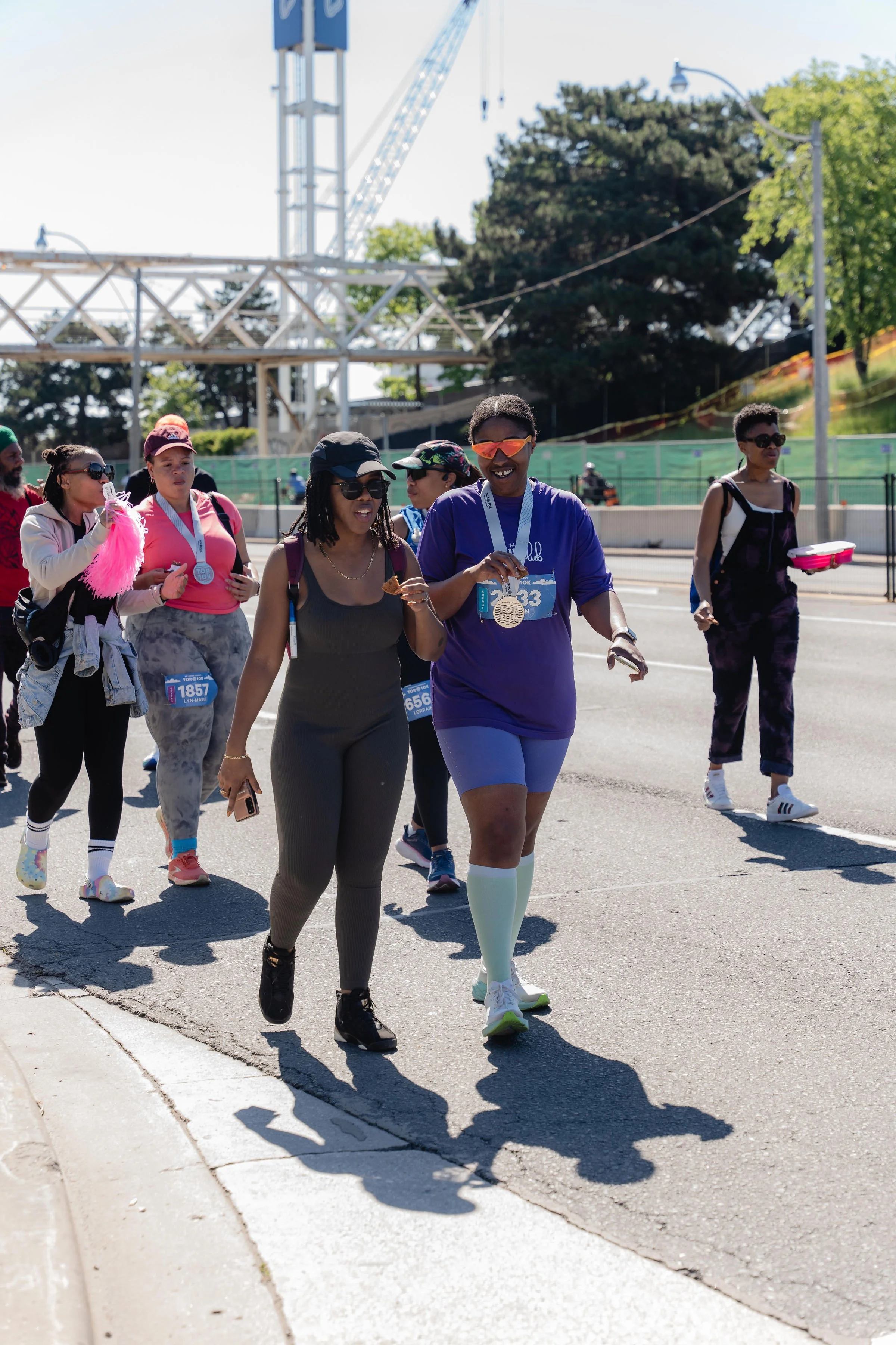 Group of runners crossing the finish line at a marathon event outdoors on a sunny day, some wearing medals.