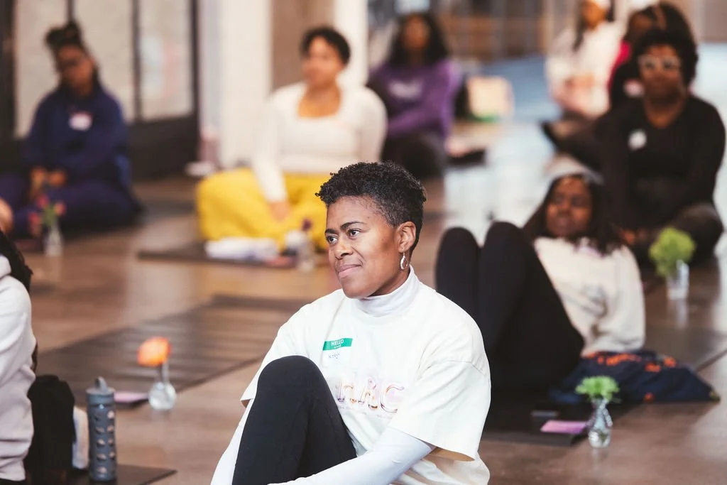 Group of women sitting cross-legged on the floor in a circle during a wellness workshop or meditation session.
