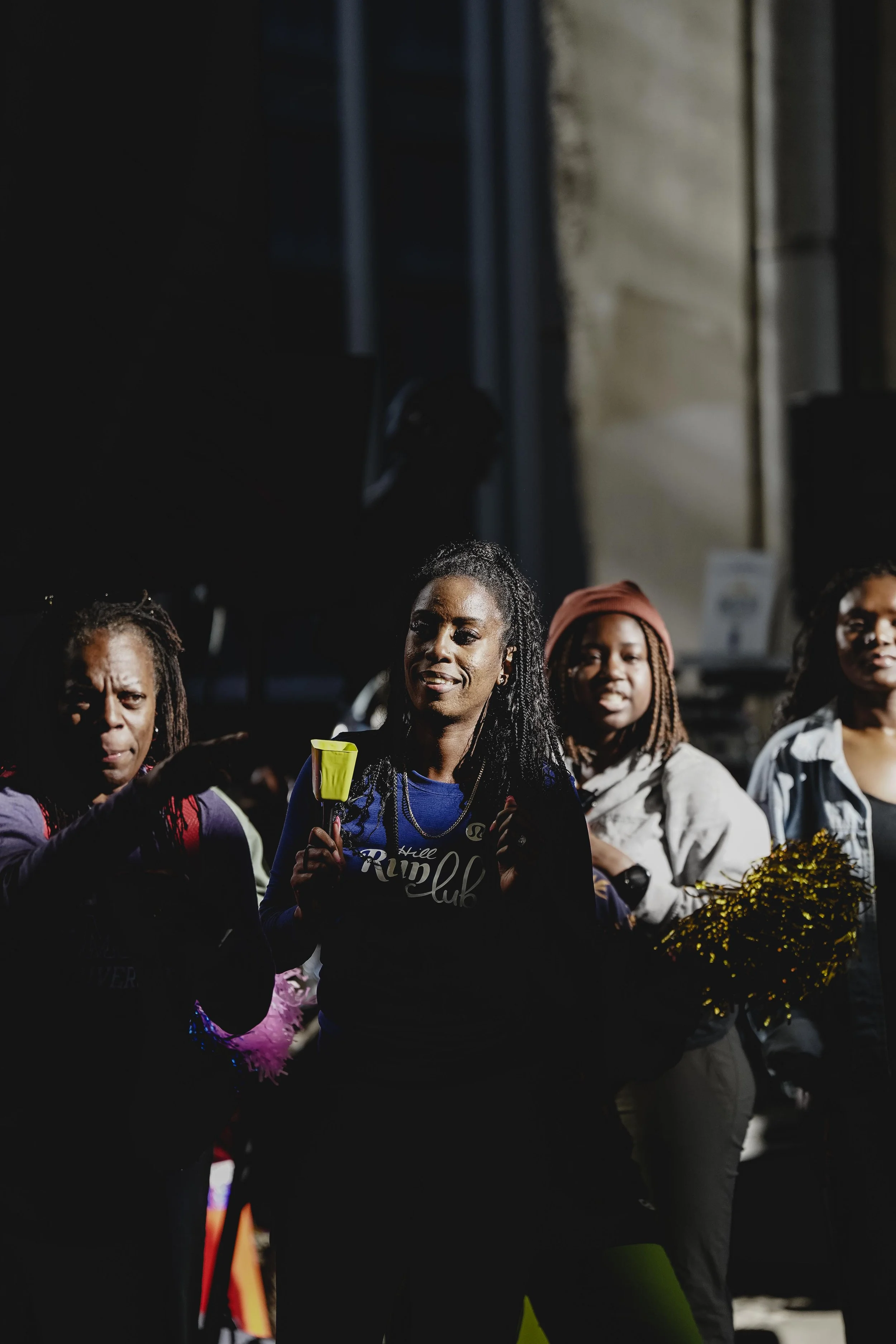 Group of women walking outdoors during nighttime, some holding pom-poms.