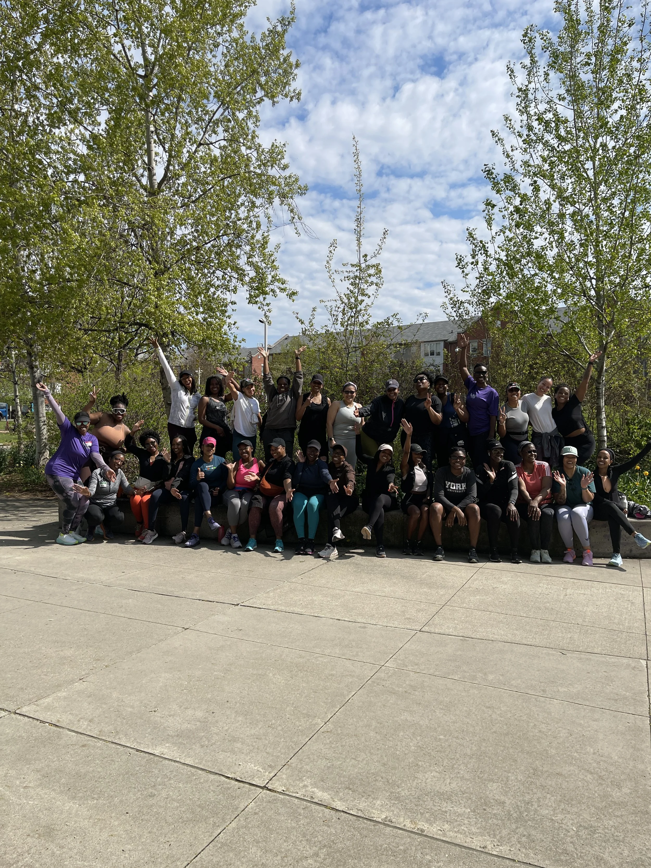 Group of diverse women posing outdoors under green trees on a sunny day.