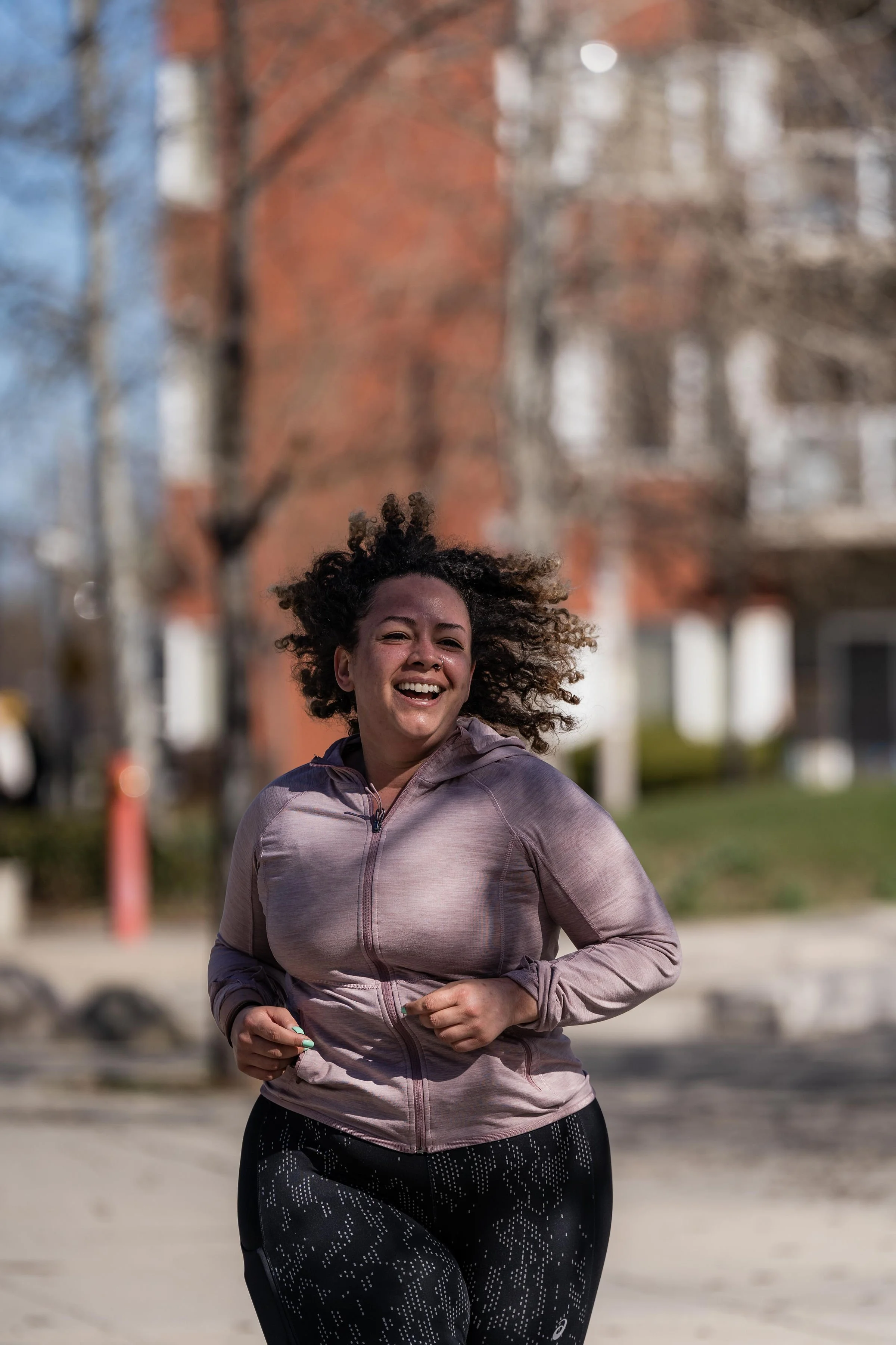 Smiling woman jogging outdoors in a residential area with trees and buildings in the background.