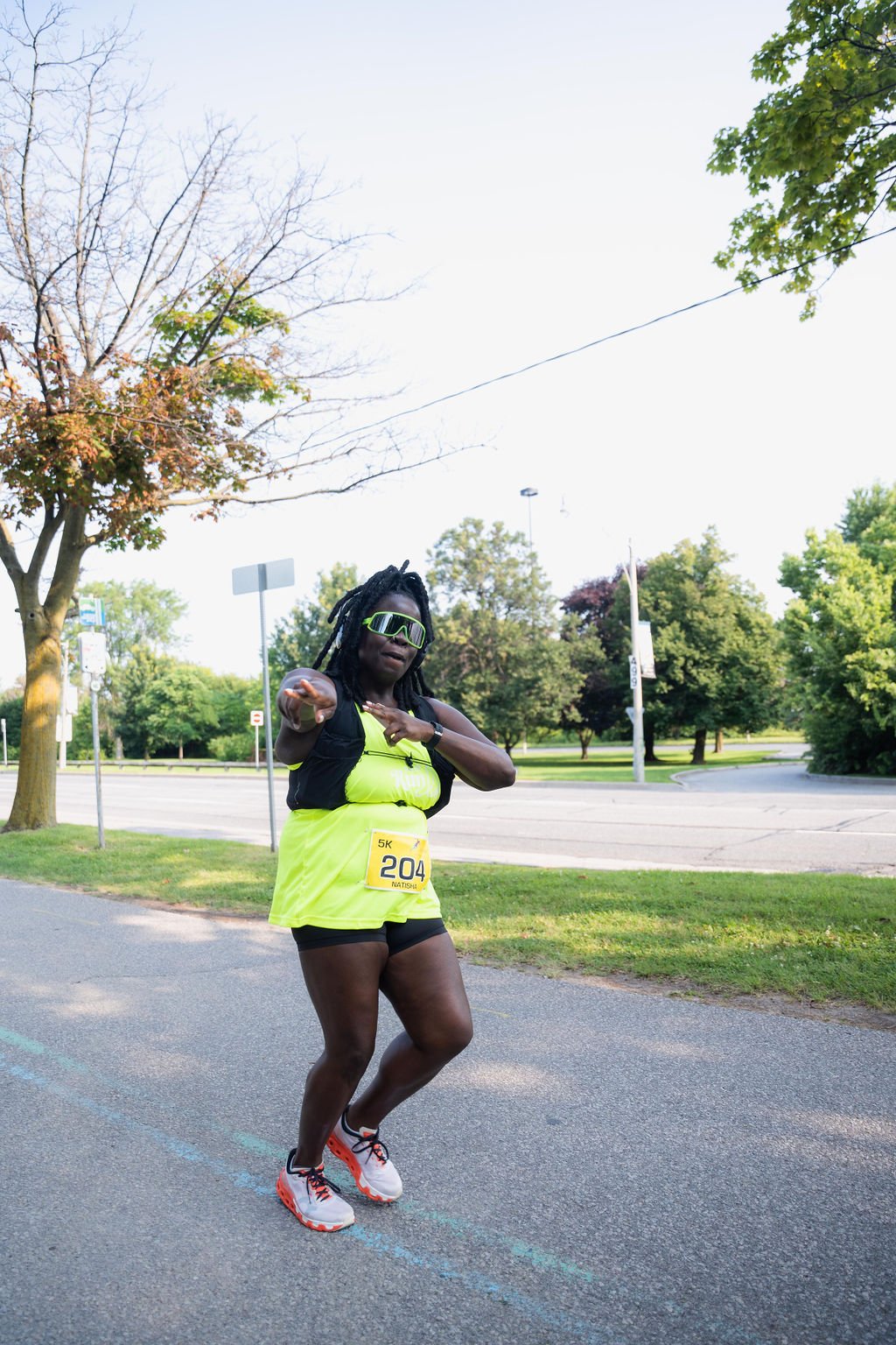 A woman in a neon yellow running outfit and sunglasses running outdoors during a race, wearing a bib number 204.
