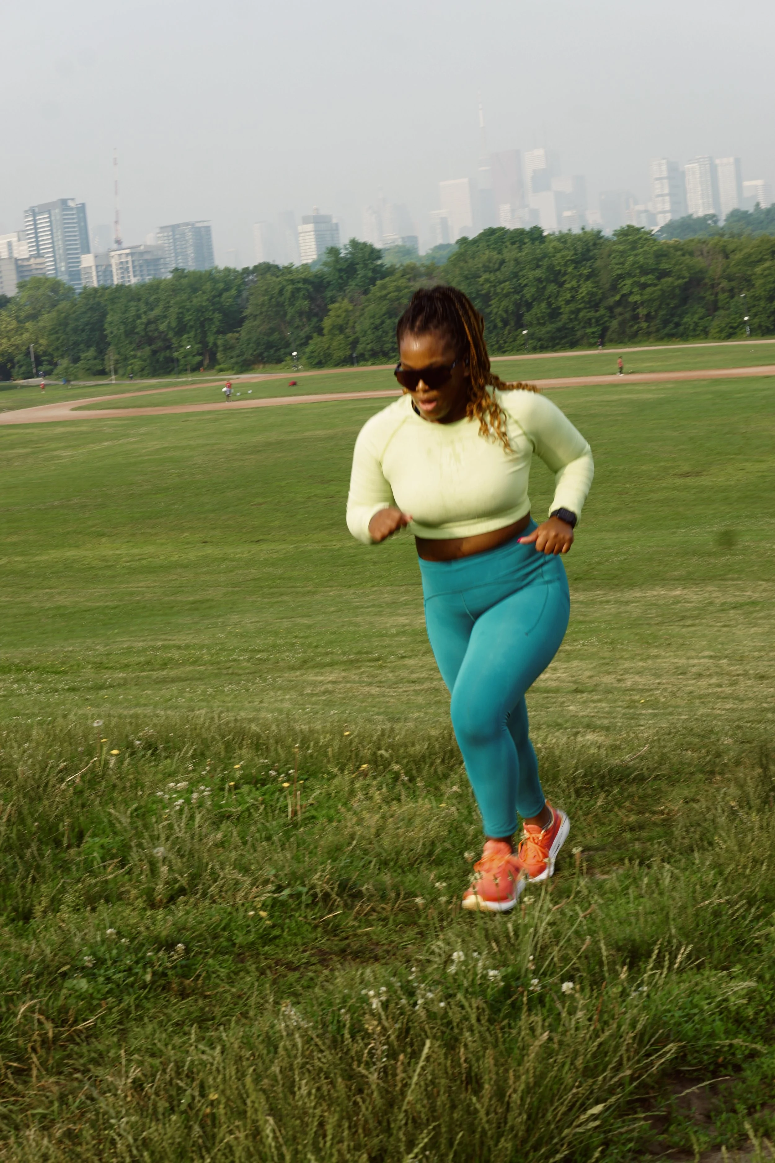 Woman running in a park with a city skyline in the background.