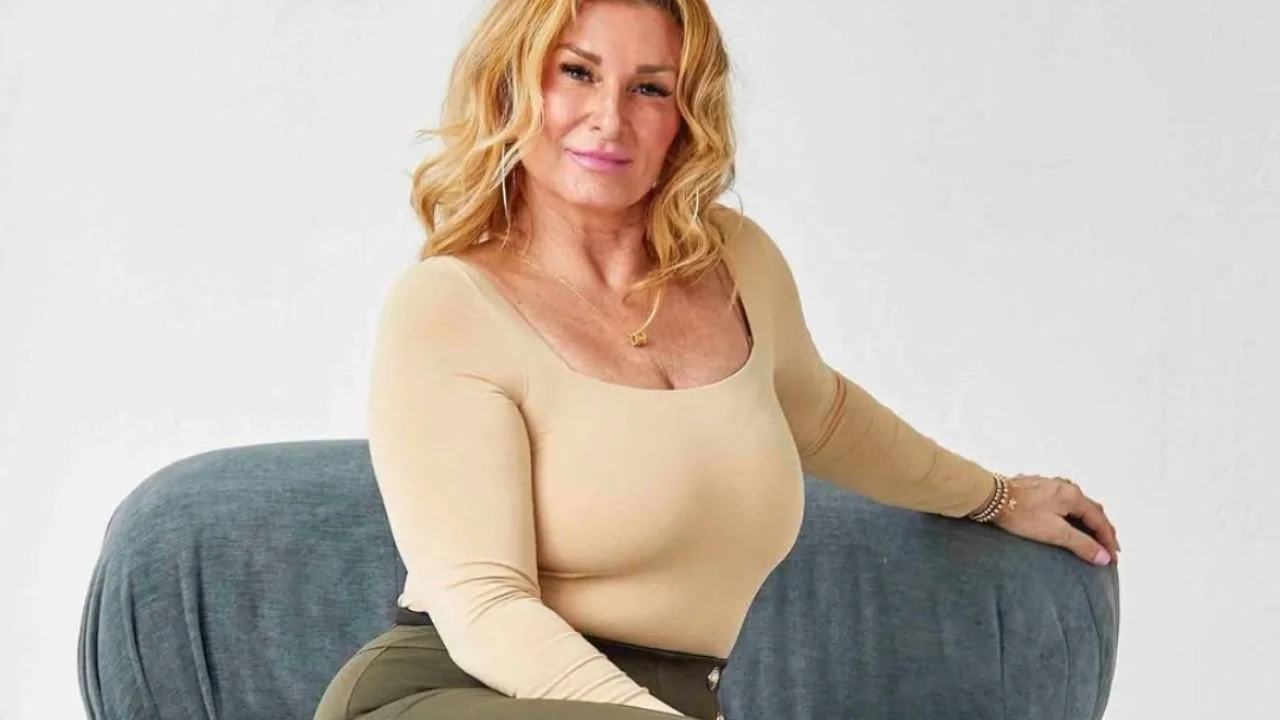 Confident blonde woman sitting on blue velvet sofa.