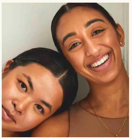 Two smiling women posing closely together, glowing skin