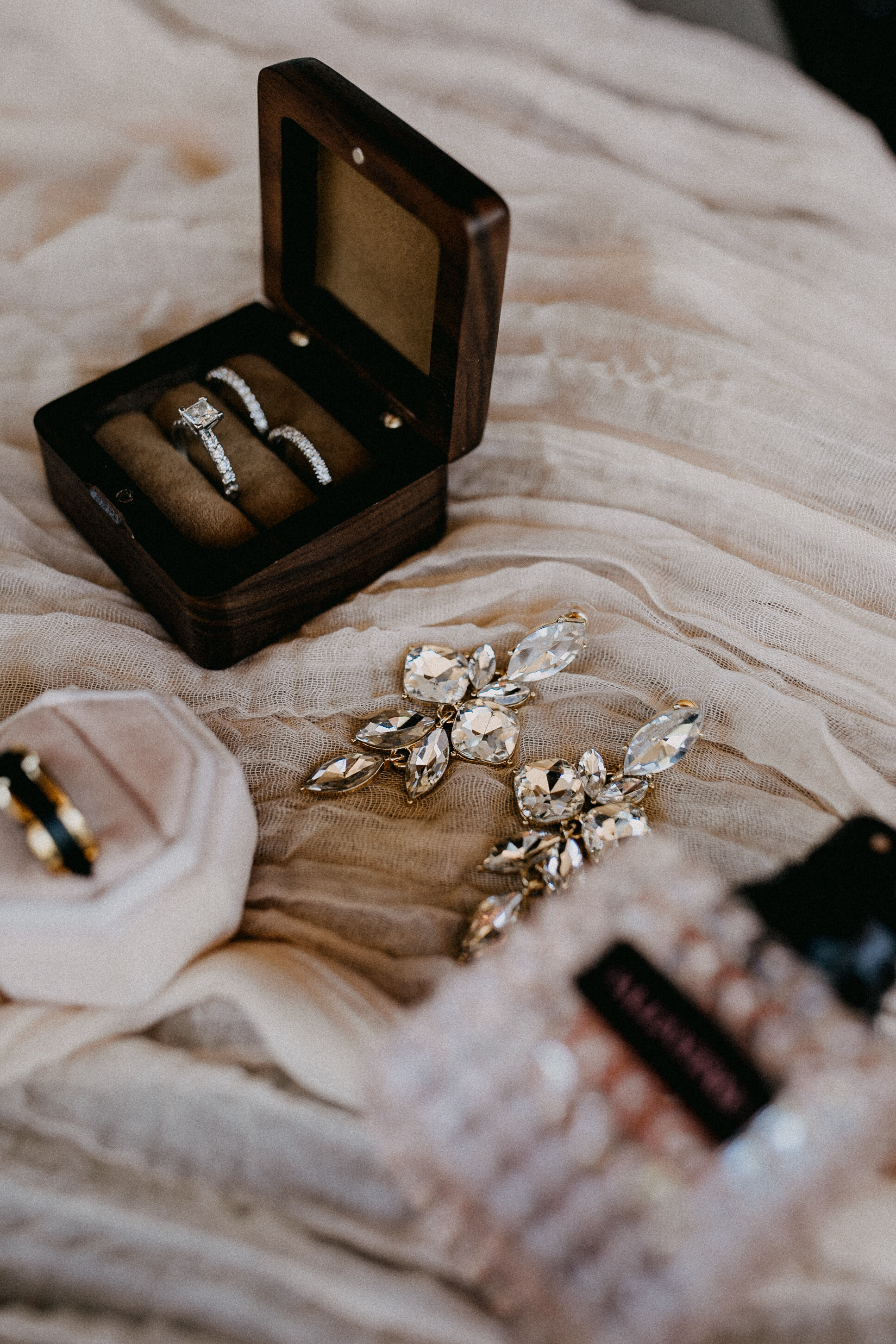 Ring box with silver rings, large crystal jewelry, and other jewelry pieces on soft fabric.