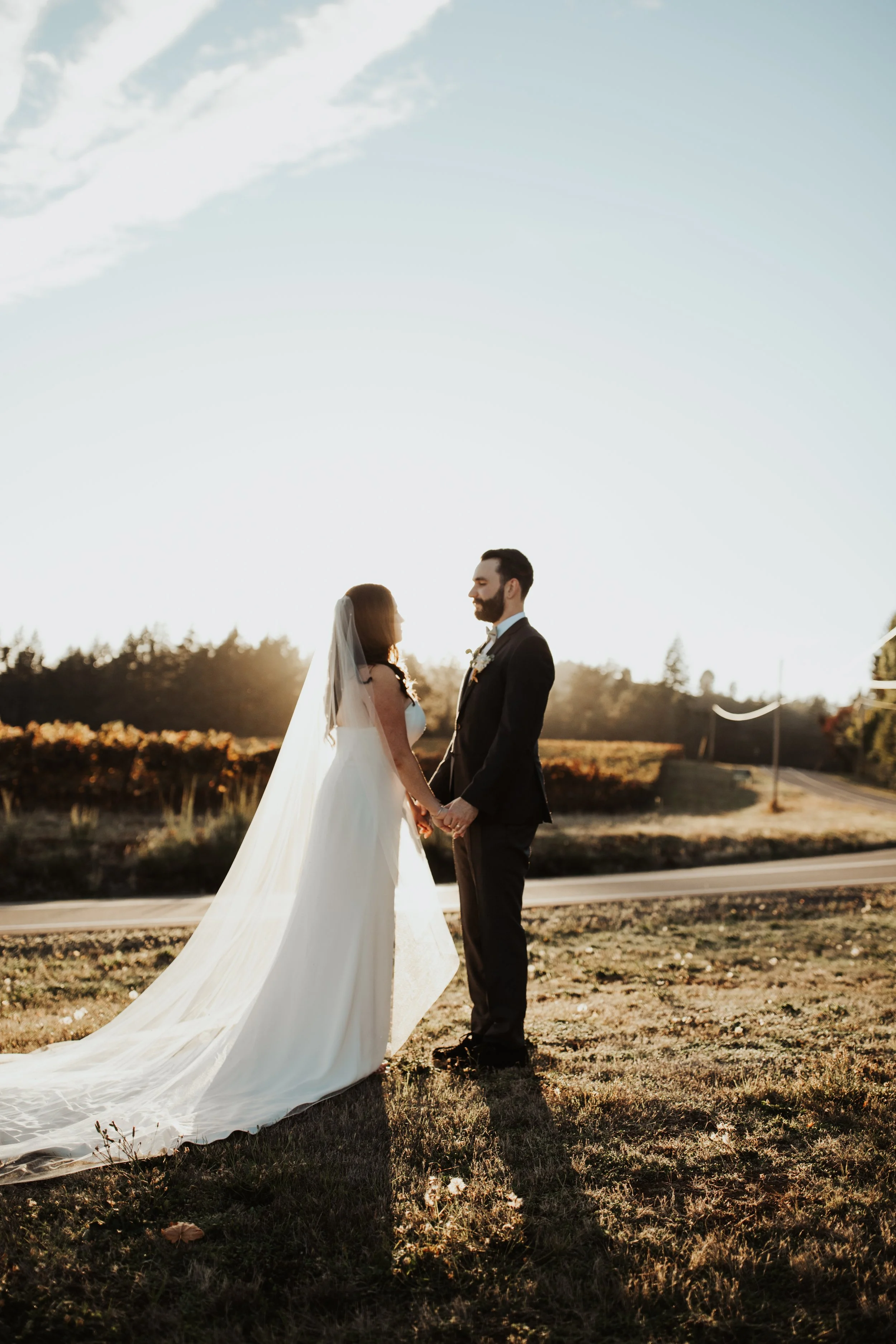 A bride and groom holding hands and facing each other outdoors during sunset. A dreamy wedding at the Gorge Crest Vineyards along the Washington Gorge  
