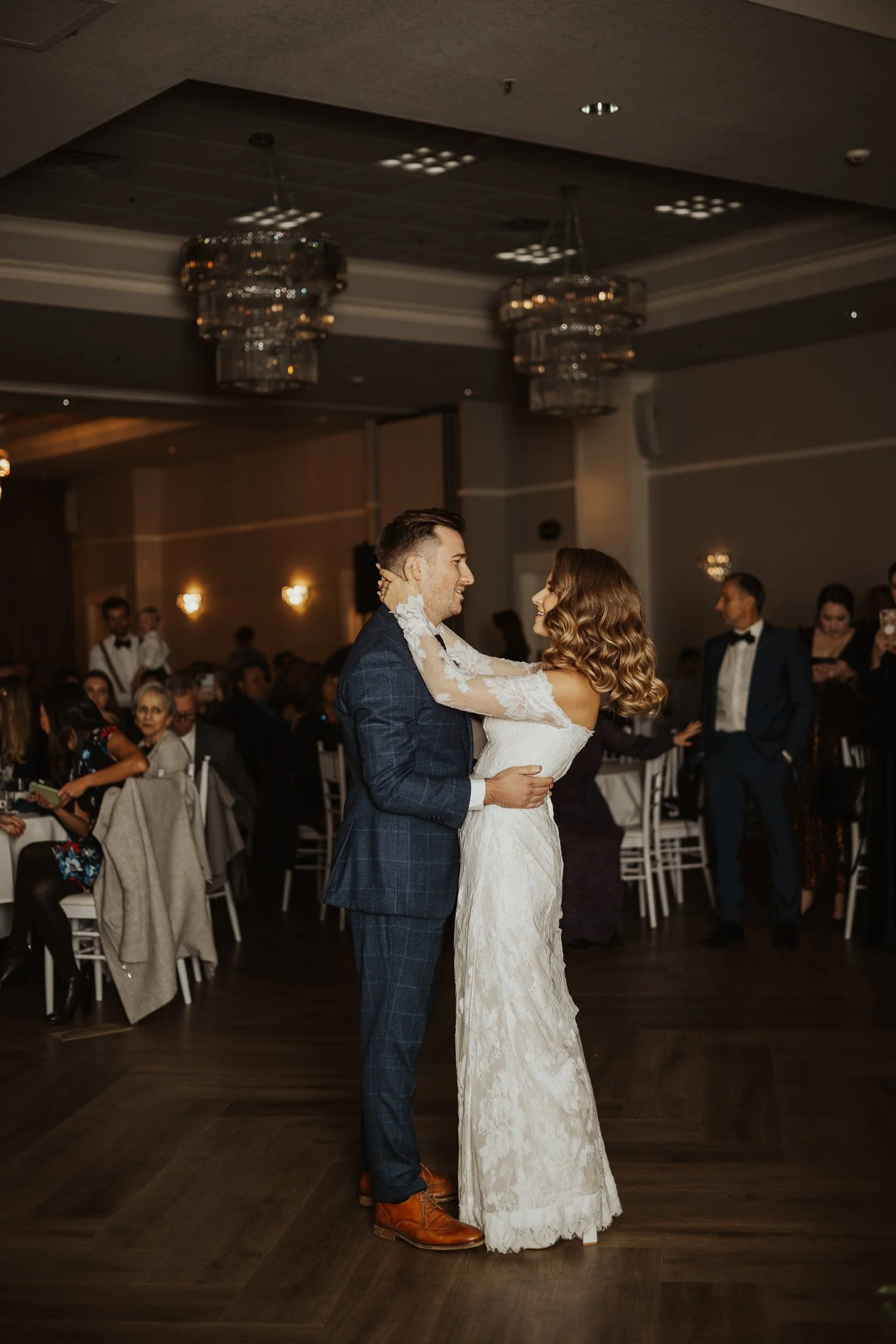 A bride and groom dancing at their wedding reception in a decorated ballroom, surrounded by seated guests.